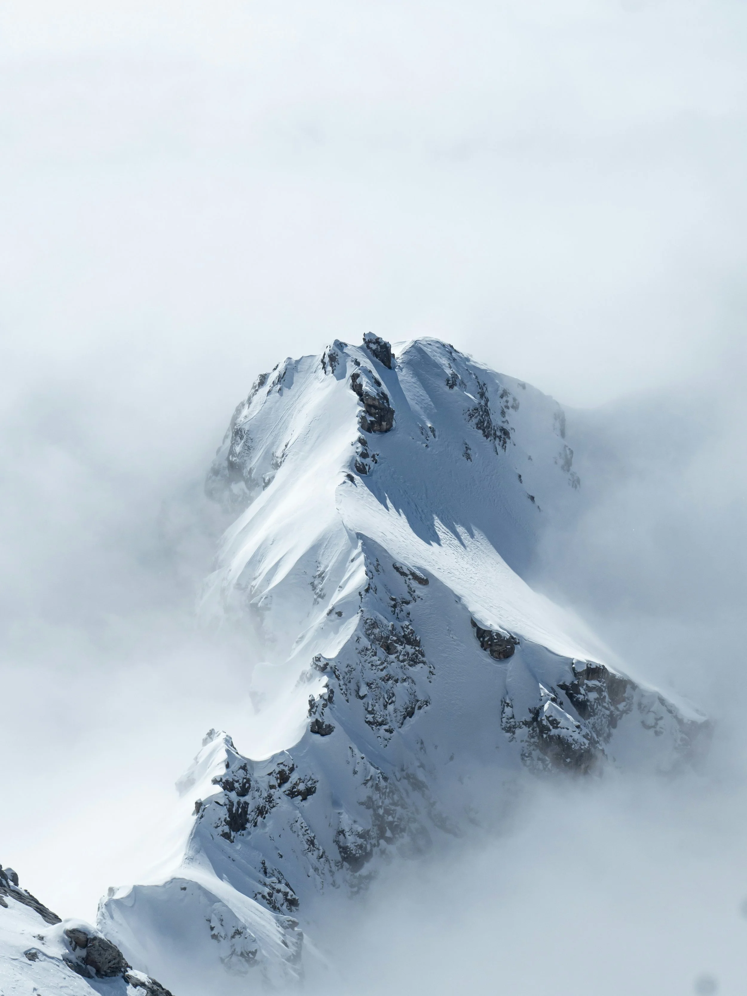 Snow-covered mountain peak surrounded by clouds and mist.