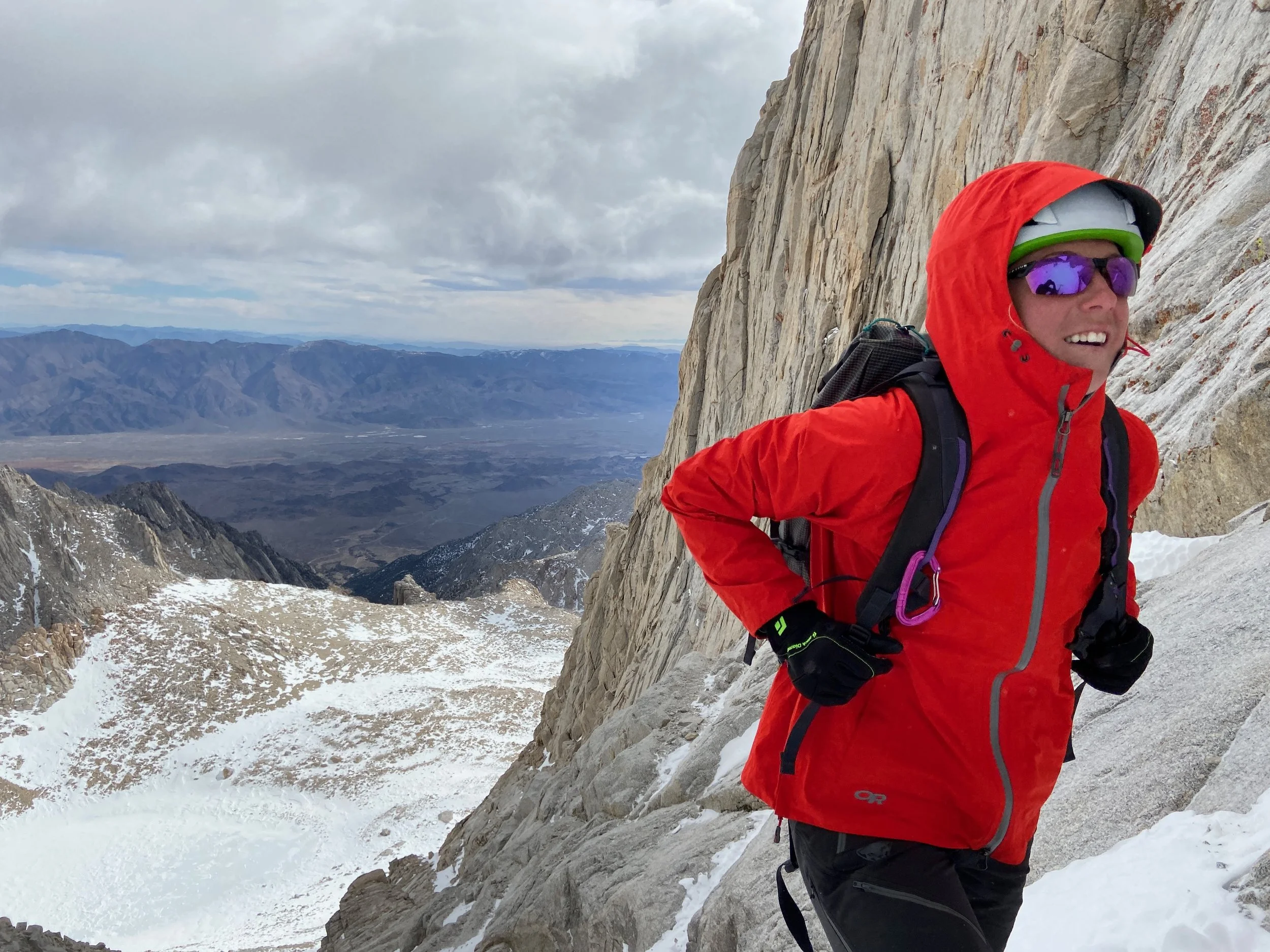 Portrait of a smiling woman with short black hair, wearing a blue top, standing amidst green plants.