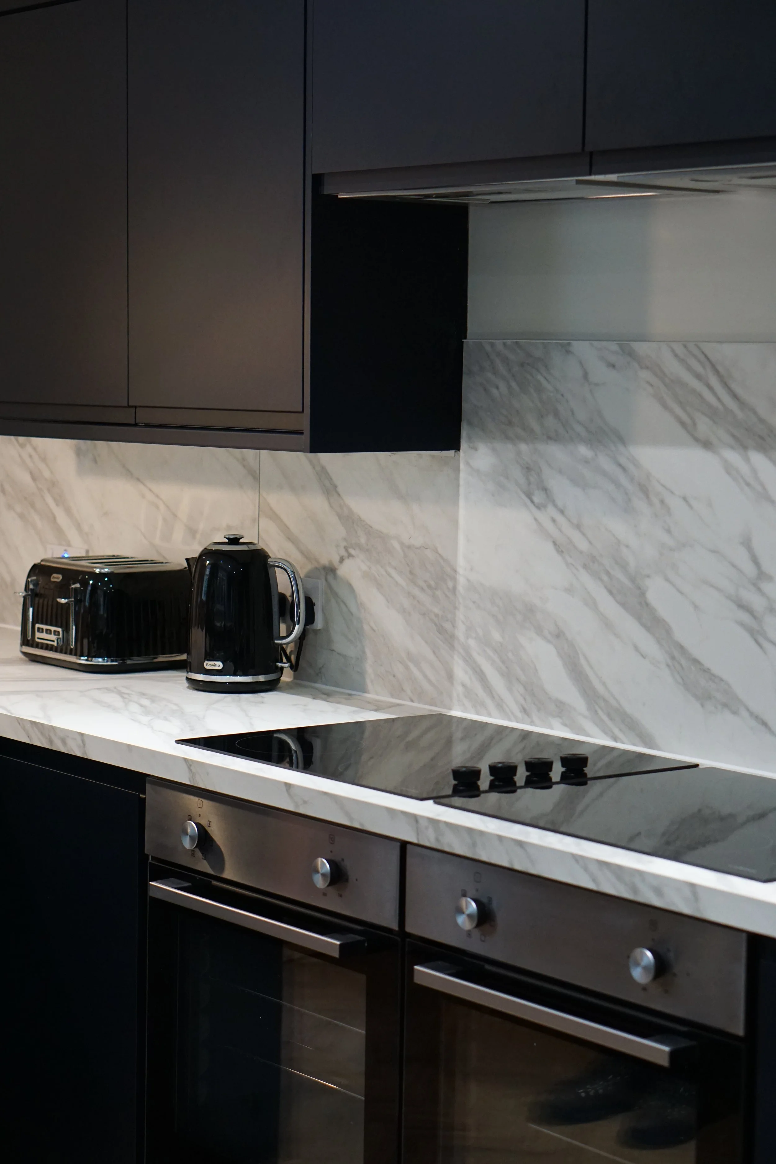 Modern kitchen with black cabinets, marble countertops and backsplash, electric stovetop, toaster, kettle, and oven.