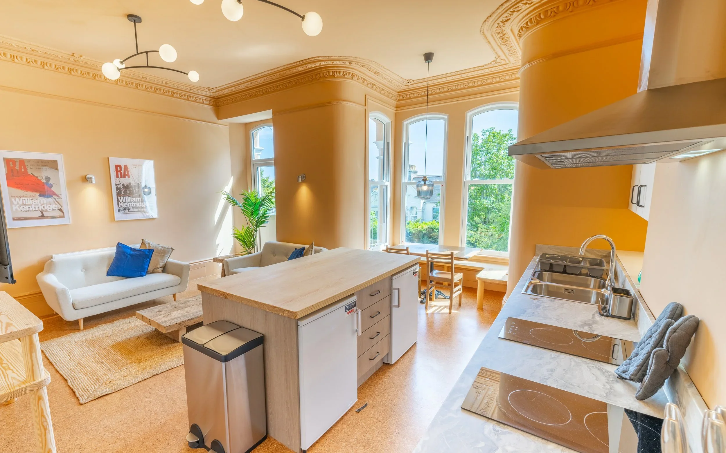 Open-concept living room and kitchen with beige walls, large windows, white sofas, a wooden island, and modern decor.