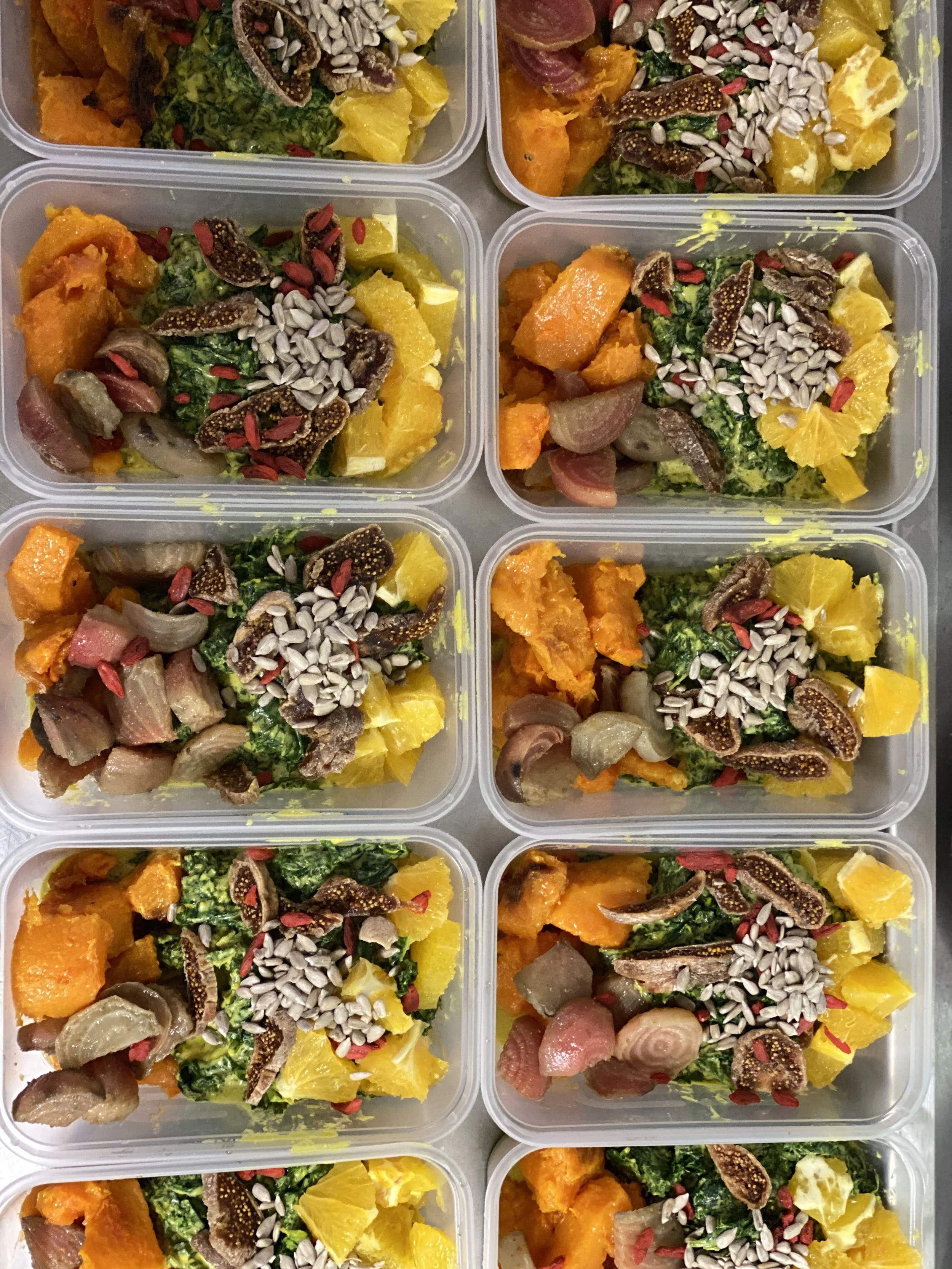 Eight meal prep containers filled with roasted sweet potatoes, greens, roasted onions, orange slices, figs, sunflower seeds, and red goji berries.