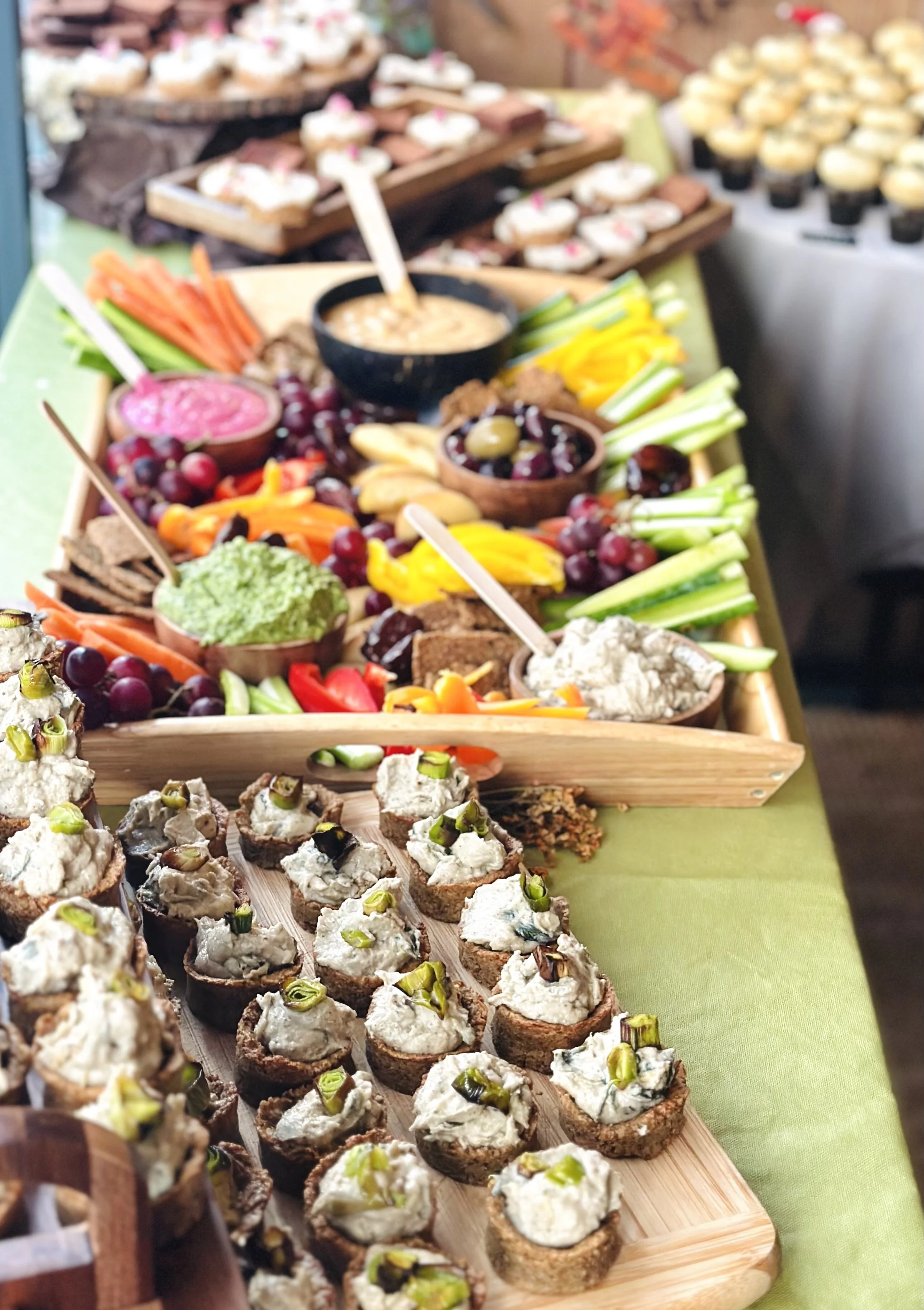 A colorful spread of appetizers including deviled eggs topped with chopped green onions, various dips, sliced vegetables, grapes, and crackers on a green tablecloth.