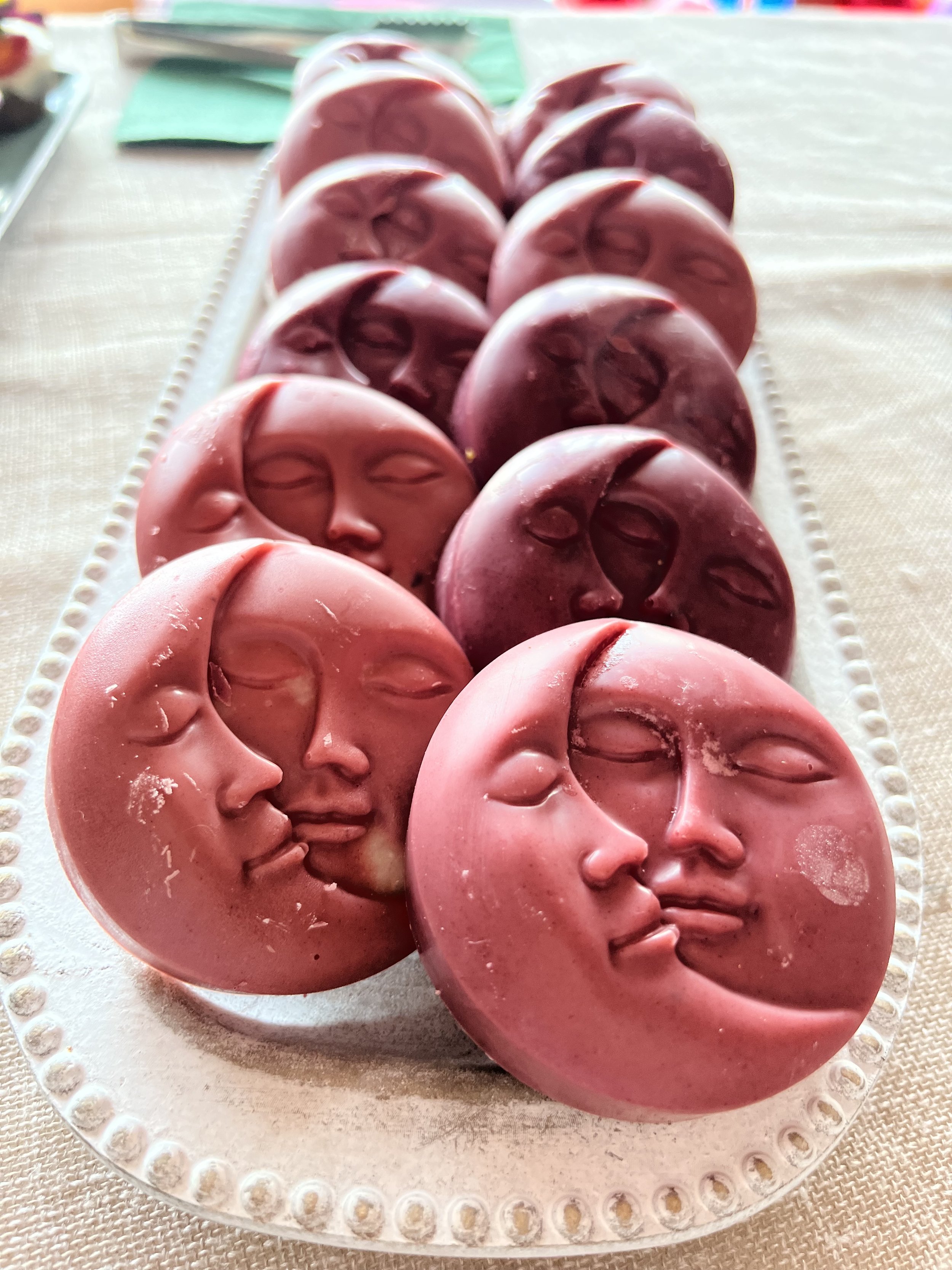 Pink and purple moon-shaped chocolates with a face profile design, arranged on a white platter.