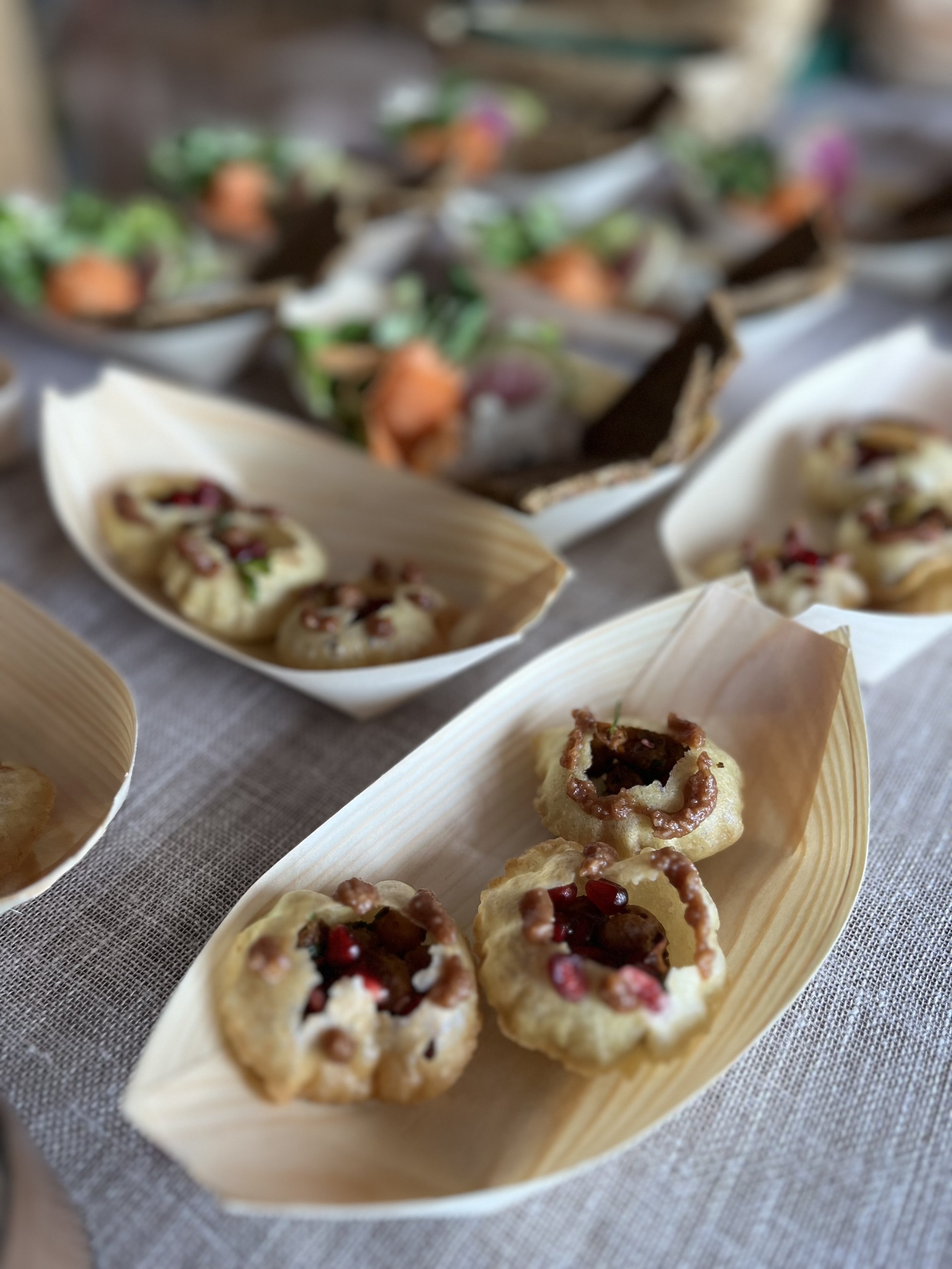 Assorted appetizers on a table, including fried cheese balls with pomegranate seeds and herbs, served in a boat-shaped dish.