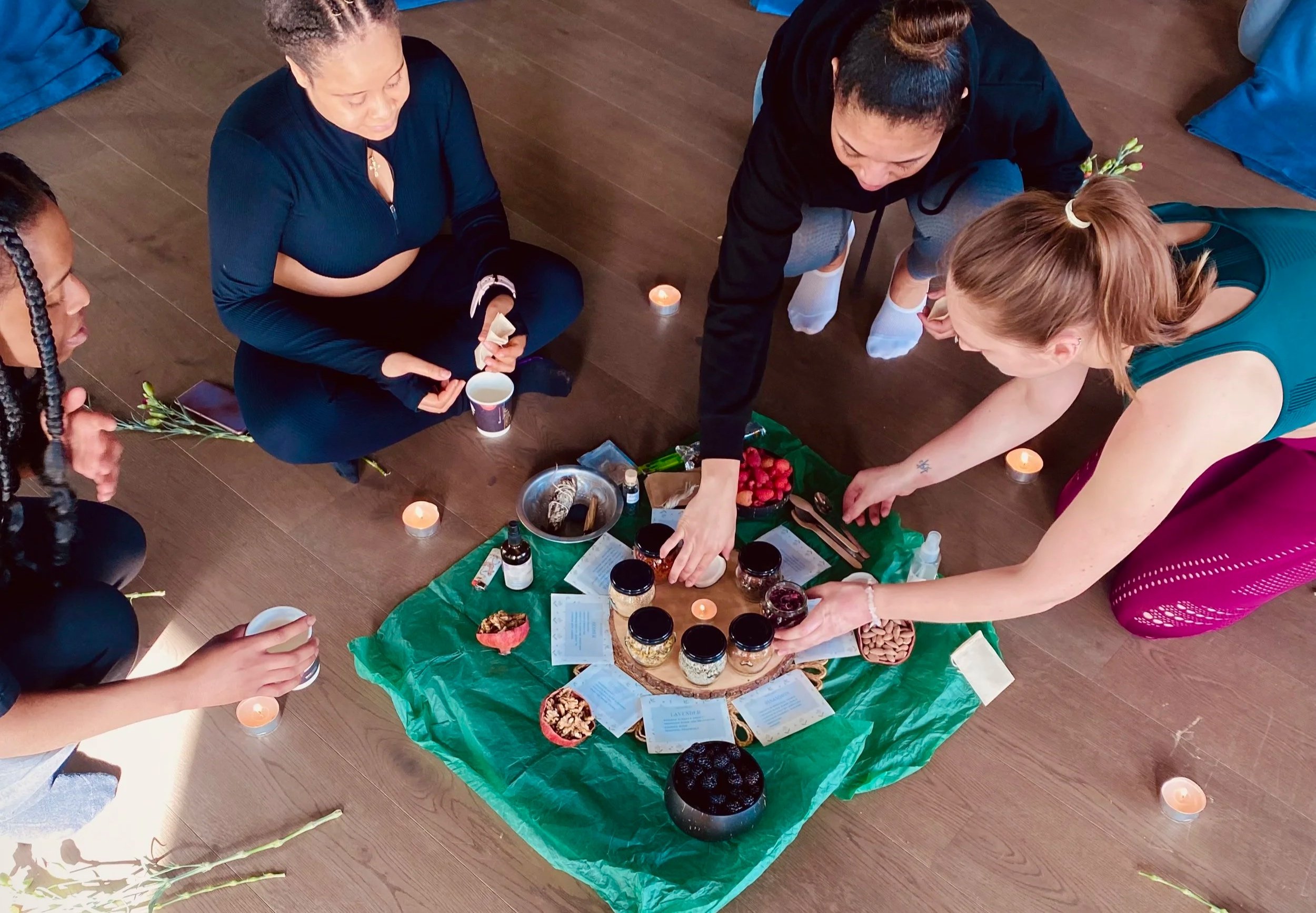 Group of people sitting on the floor around a display of various jars and bowls with natural items and papers, with candles around the display.