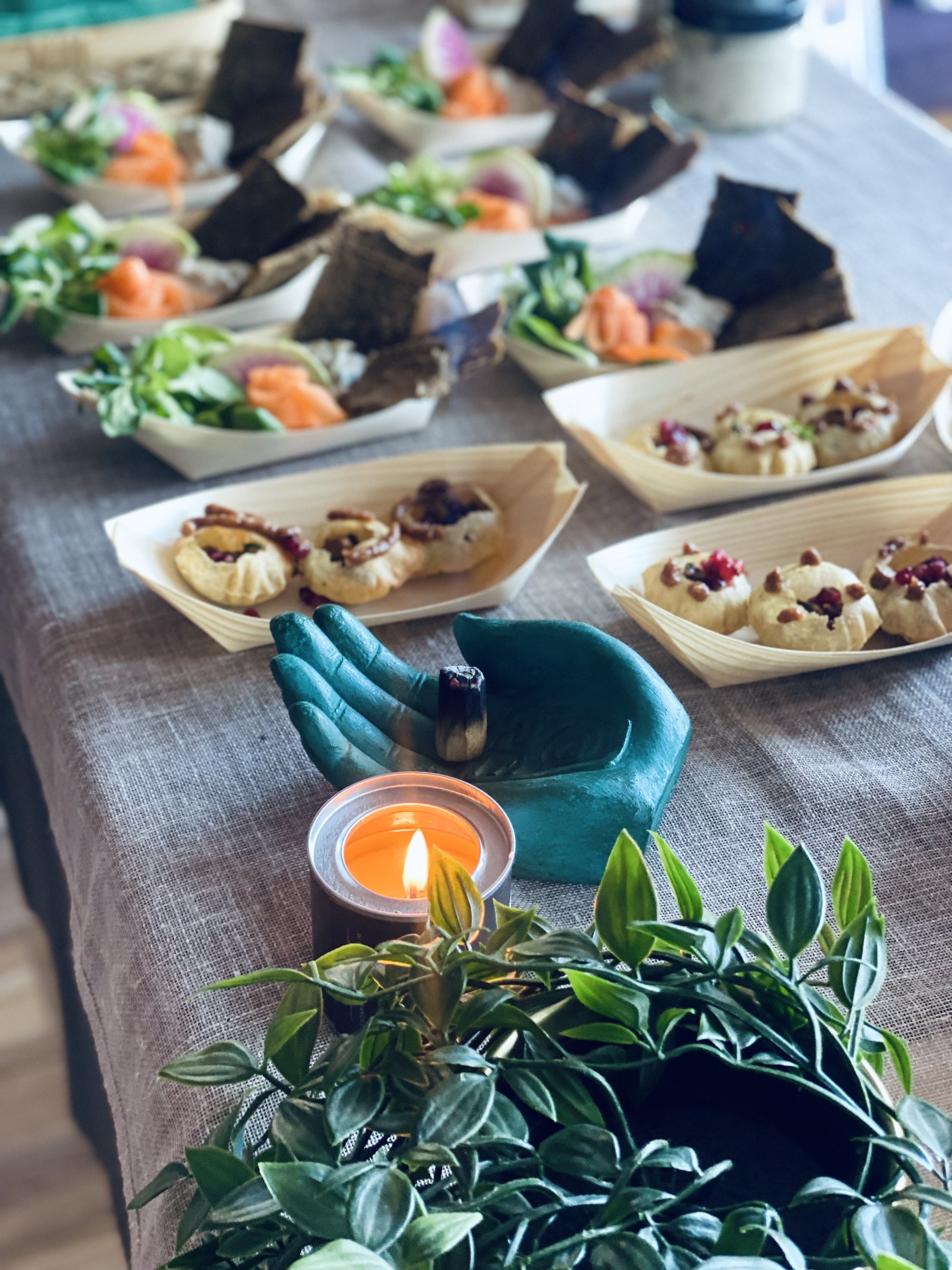 Assorted appetizers and desserts on a table with a lit candle, teal-colored statue, and green plant in the foreground.