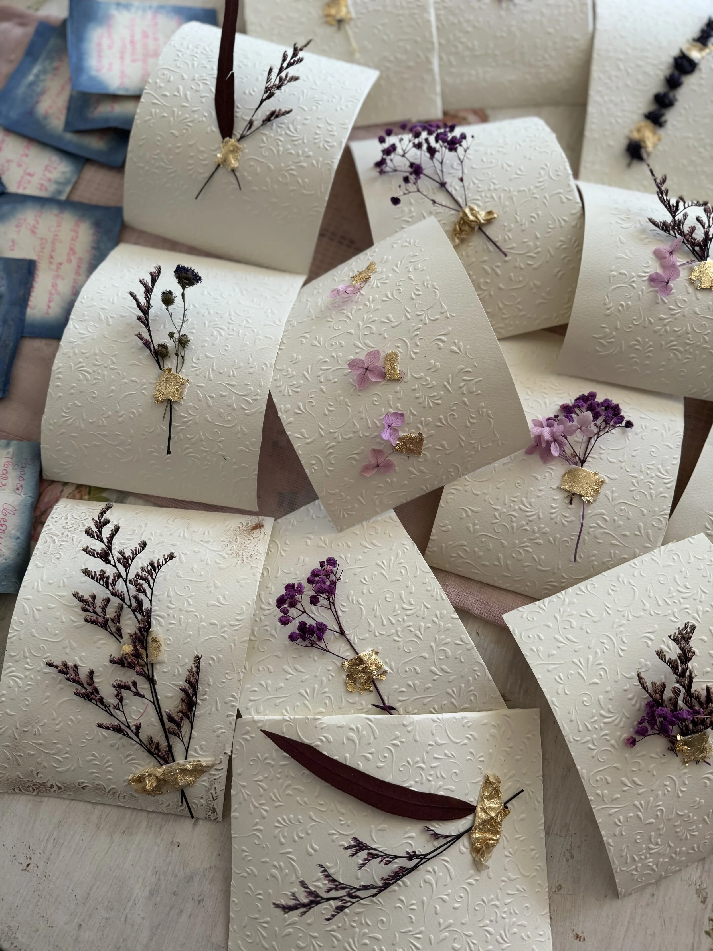 Decorative white cards with embossed patterns, adorned with dried purple and pink flowers and gold accents.