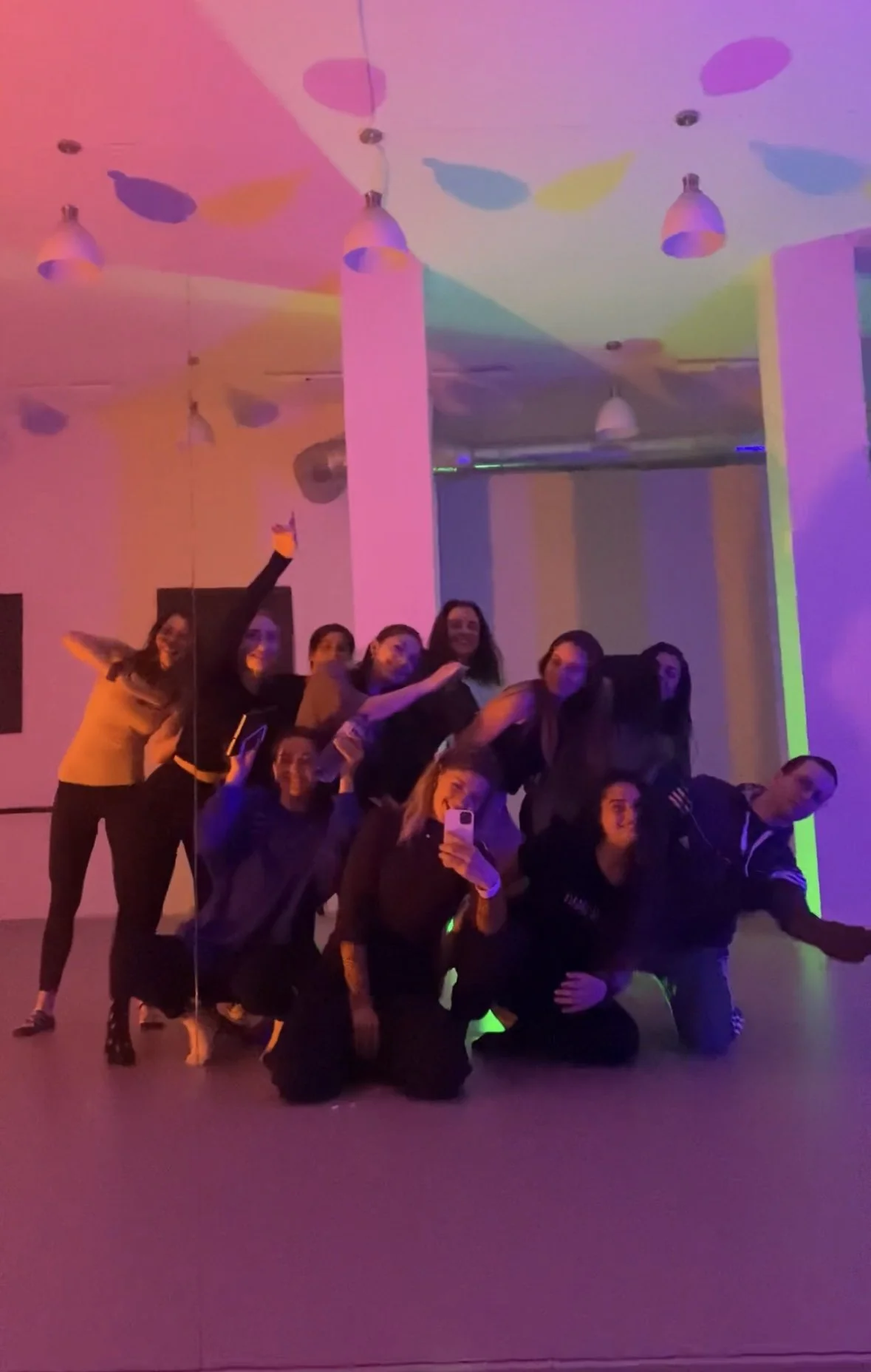 Group of people taking a selfie in a room with colorful, neon lighting and disco ball reflections on the ceiling.