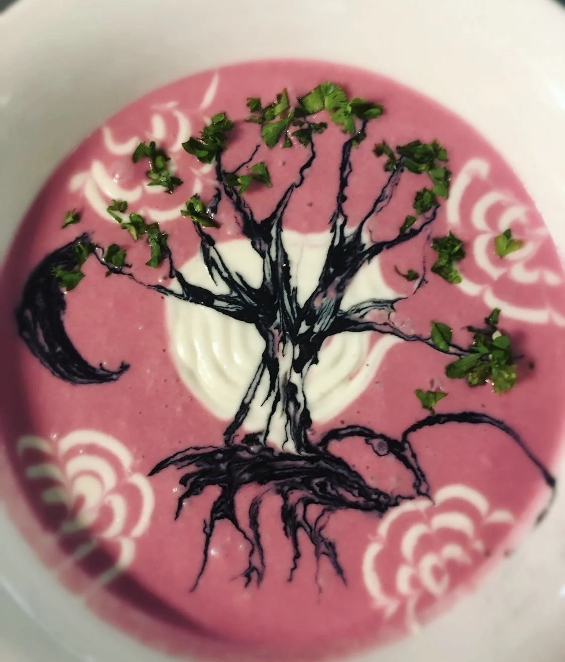 Pink and white soup with a black tree design drawn on top, garnished with chopped green herbs.