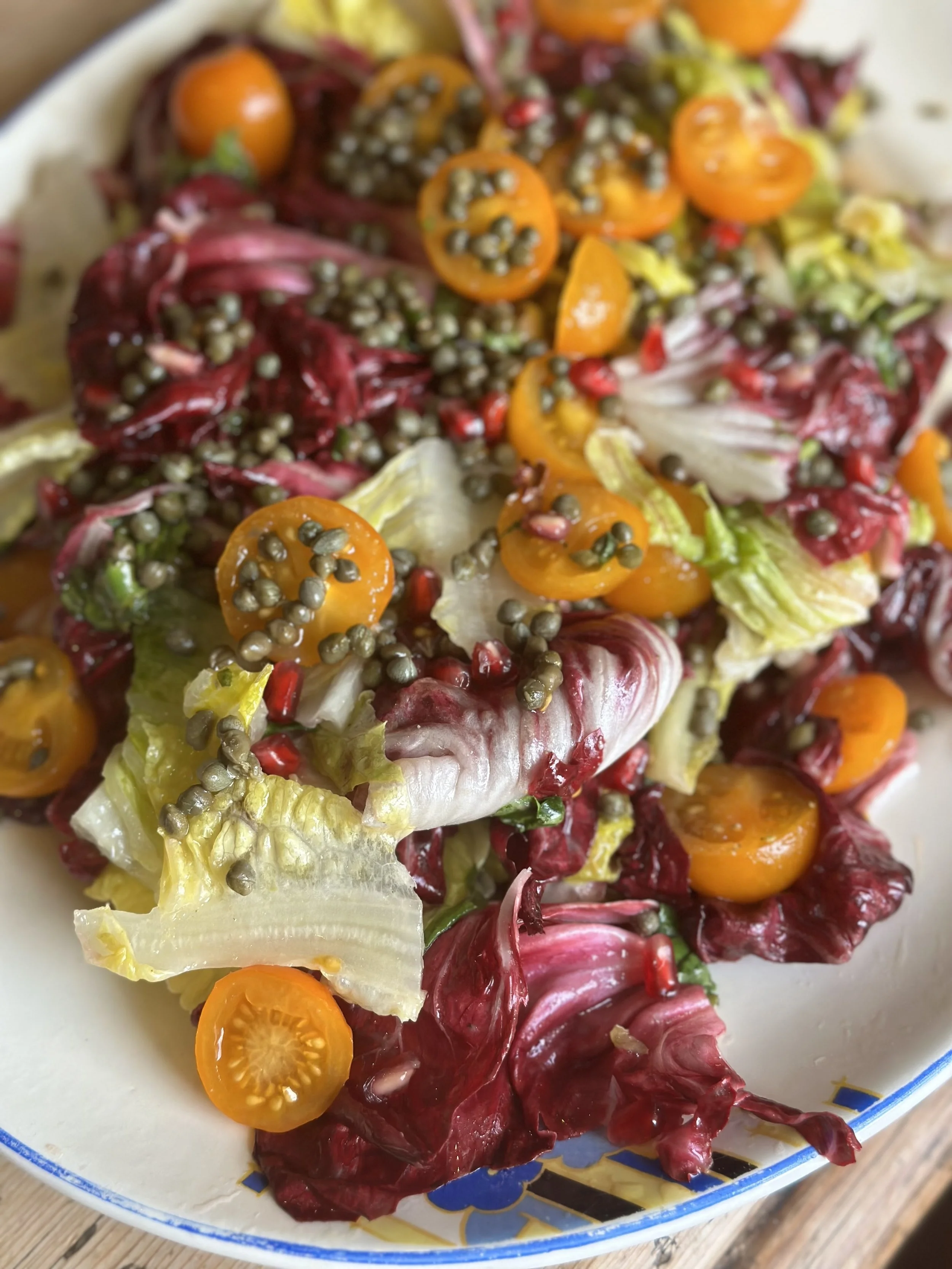 Mixed salad with romaine and radicchio lettuce, yellow cherry tomatoes, and black pepper scattered on top, served on a white plate with a decorative blue and gold rim.