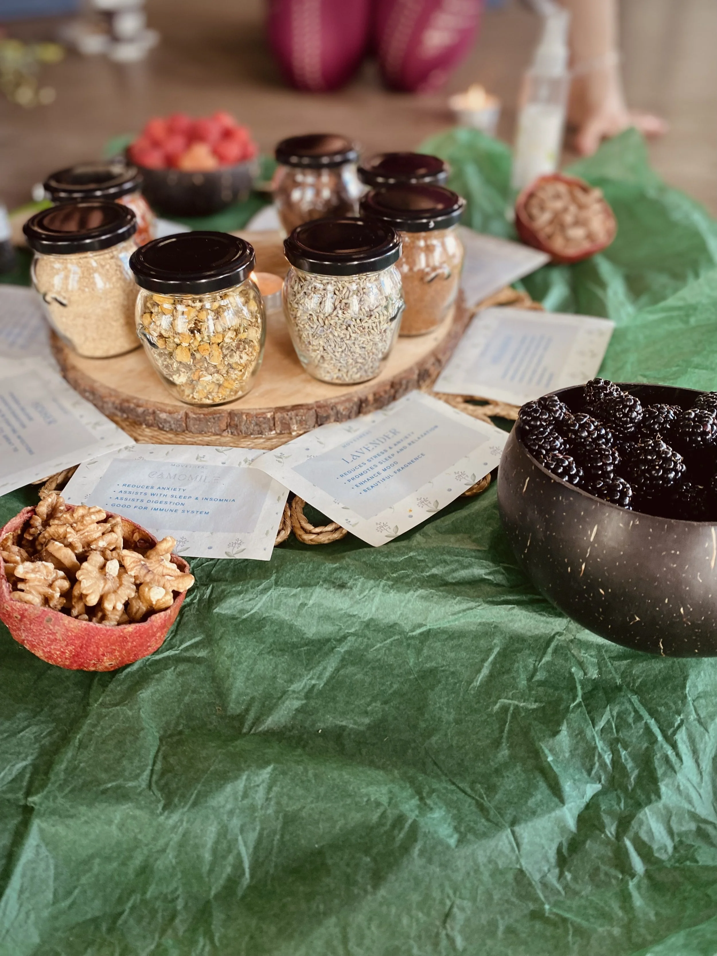 Arrangement of small jars, bowls of blackberries, walnuts, and honey on a table with green tissue paper and informational cards.