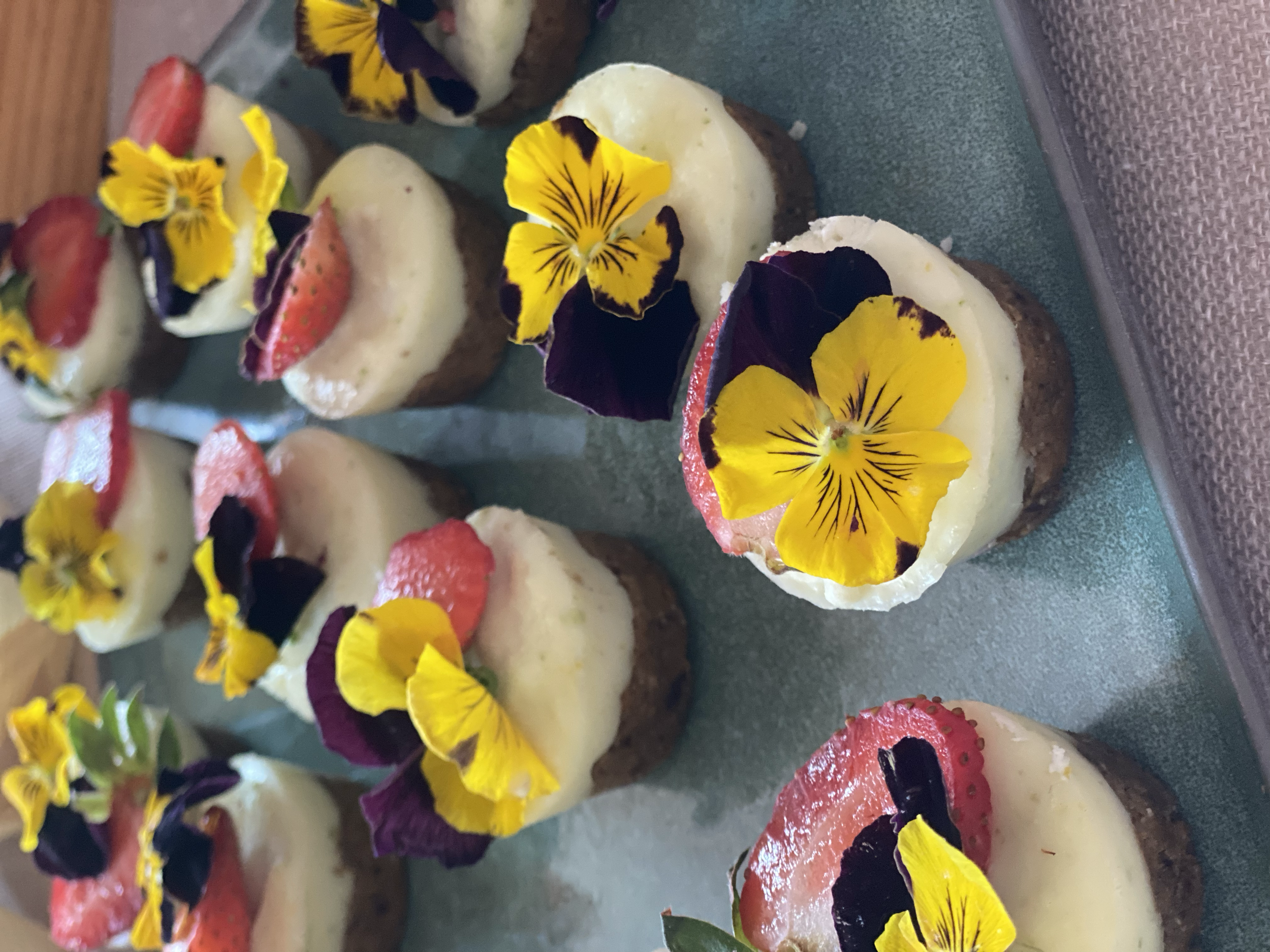 Dessert cups topped with strawberries, edible flowers, and dark chocolate garnish, served on a tray.
