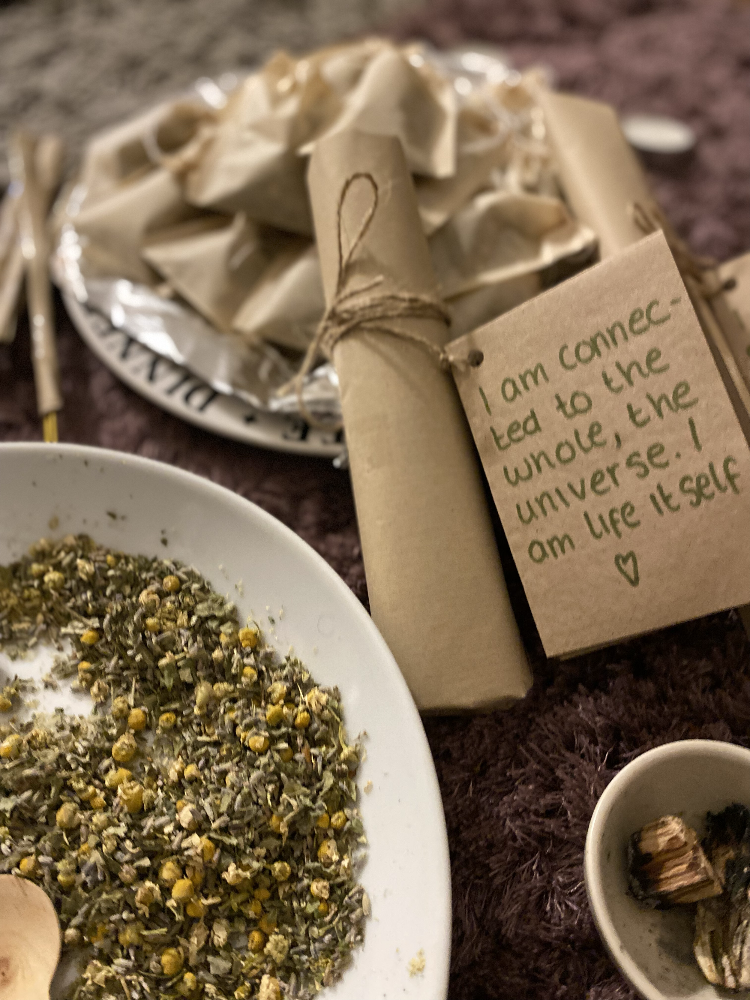 Various small bundles wrapped in parchment paper, a handwritten note attached, a white plate with dried herbs, and a small cup with herbs.