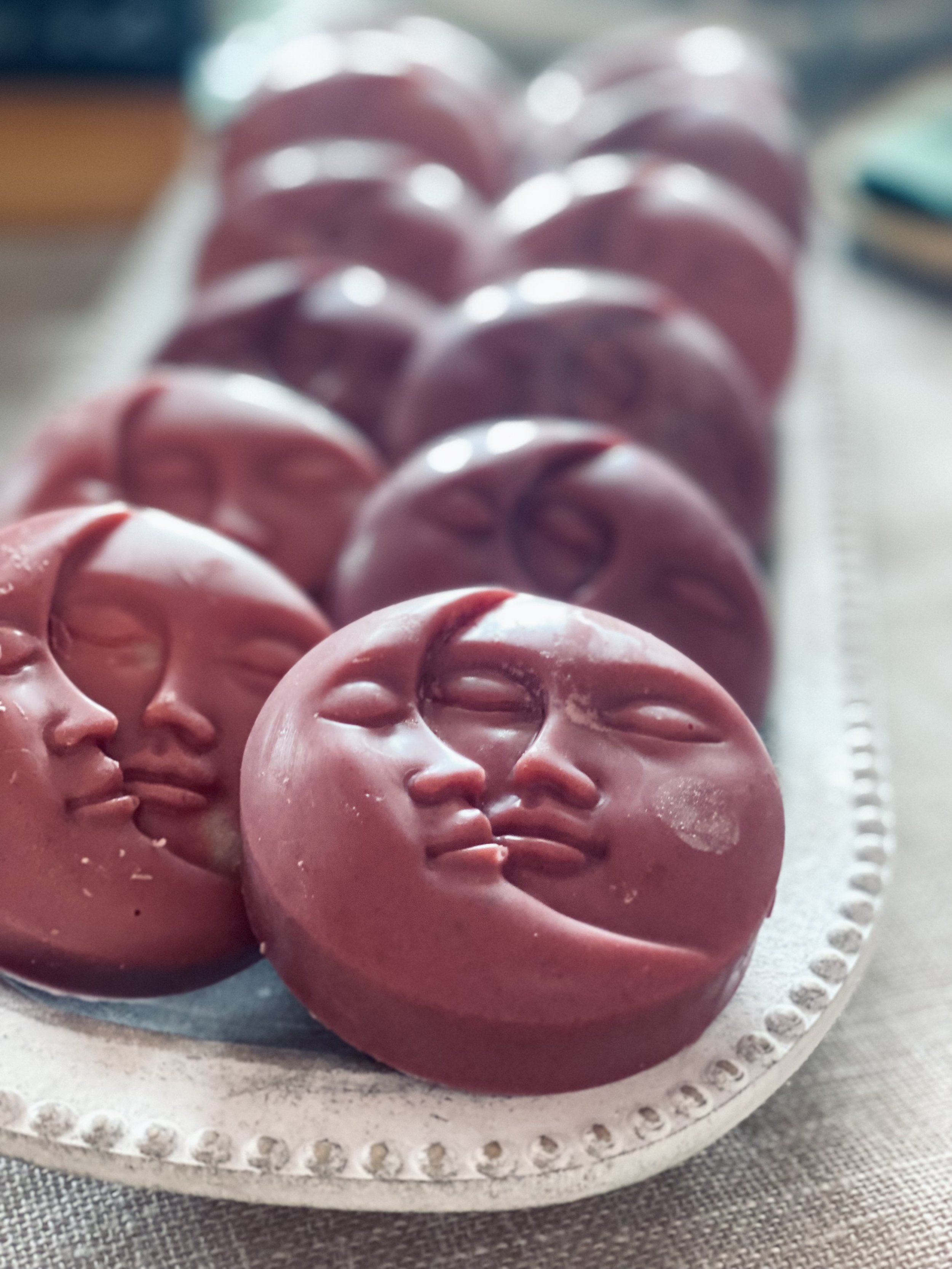 Pink moon-shaped soaps with a carved face of a woman and a man, arranged on a silver platter.