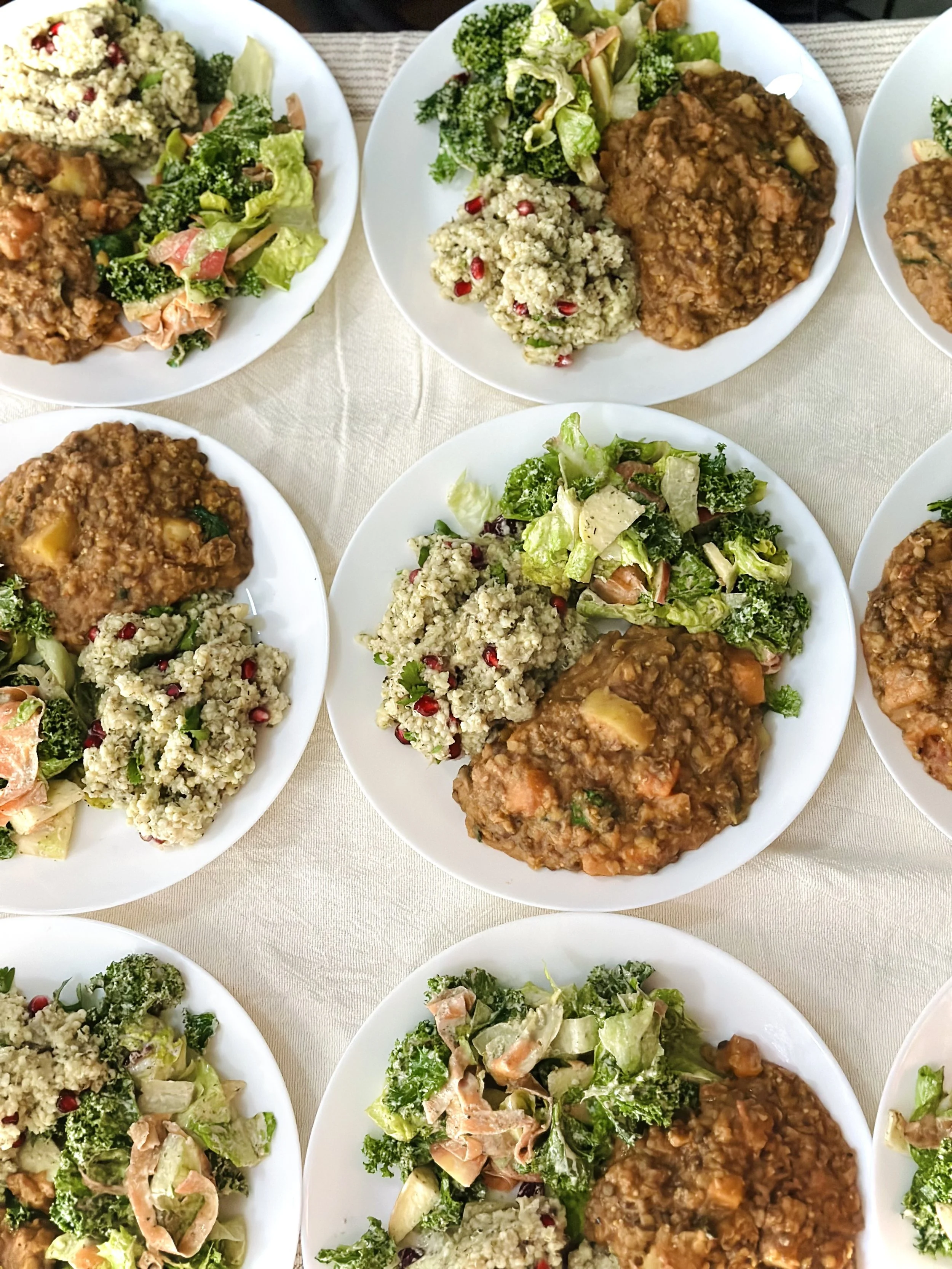 Plates of salad, couscous, and chili with meat and vegetables on a white tablecloth.