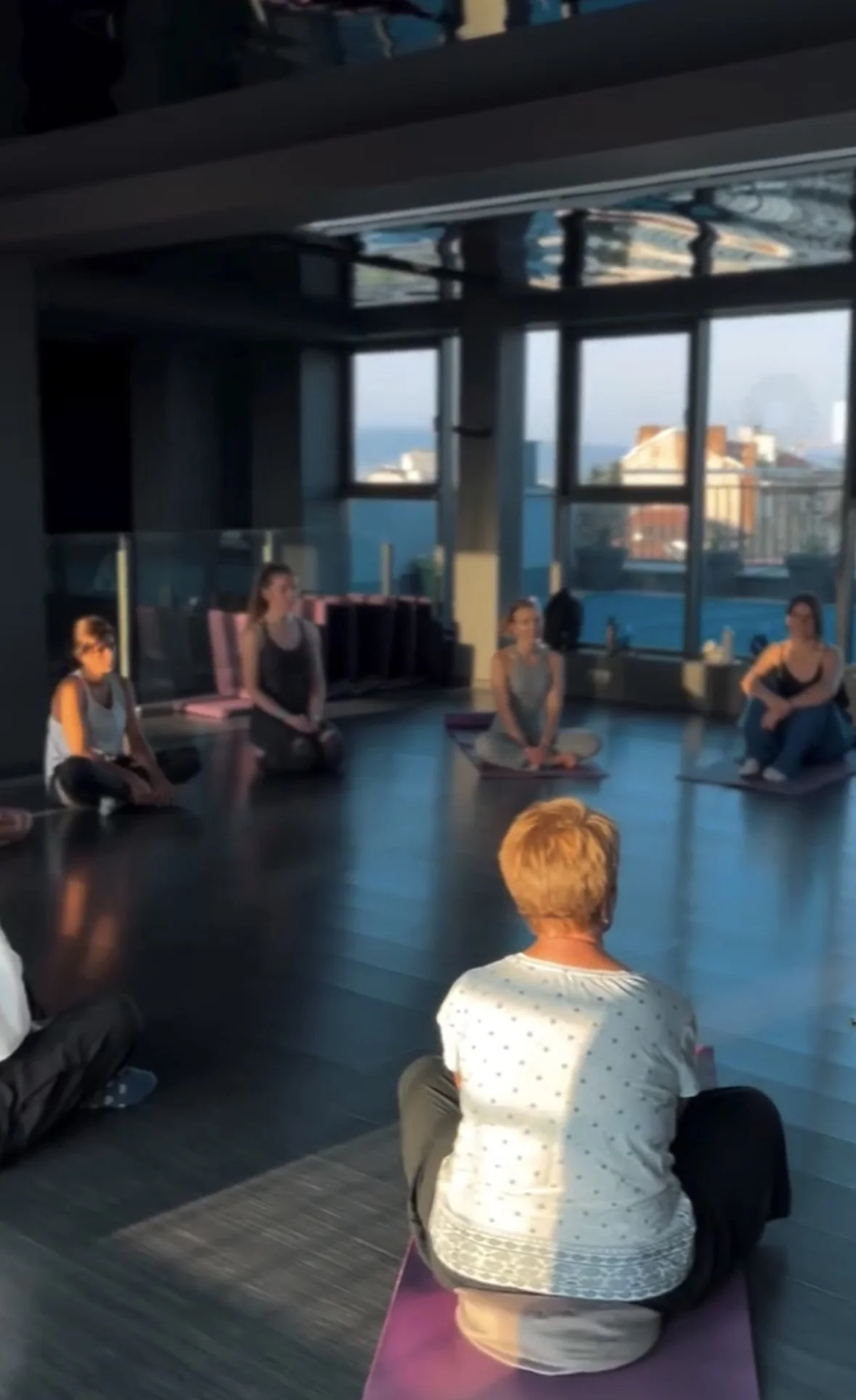 People participating in a yoga or meditation class in a high-rise studio with large windows and city views.