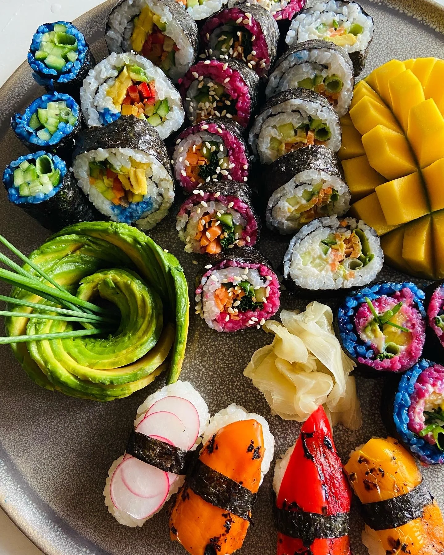 Assorted colorful sushi rolls, sliced mango, and vegetables on a platter.