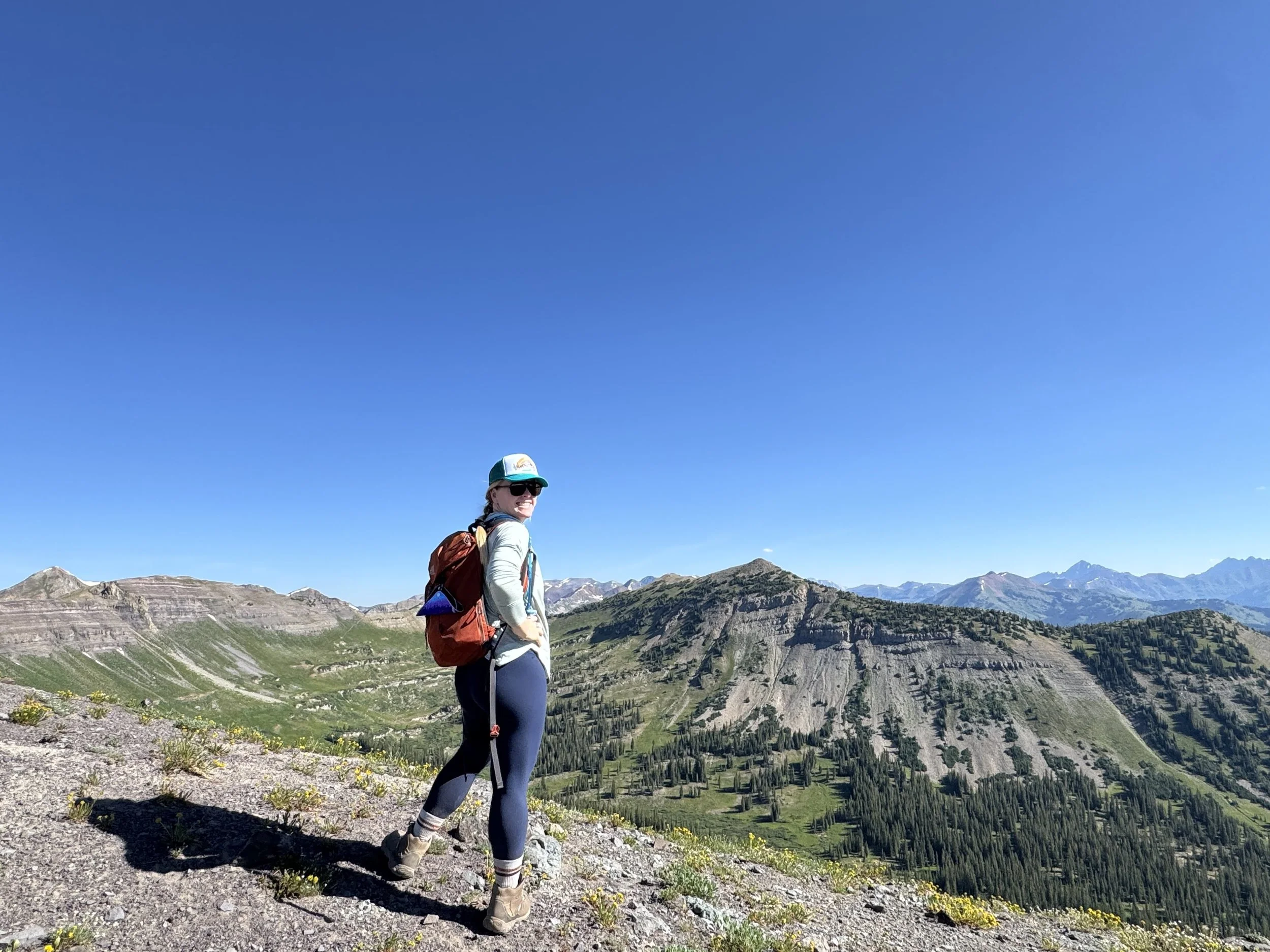 Kat Libby wellness coach hiking with mountain peaks behind her