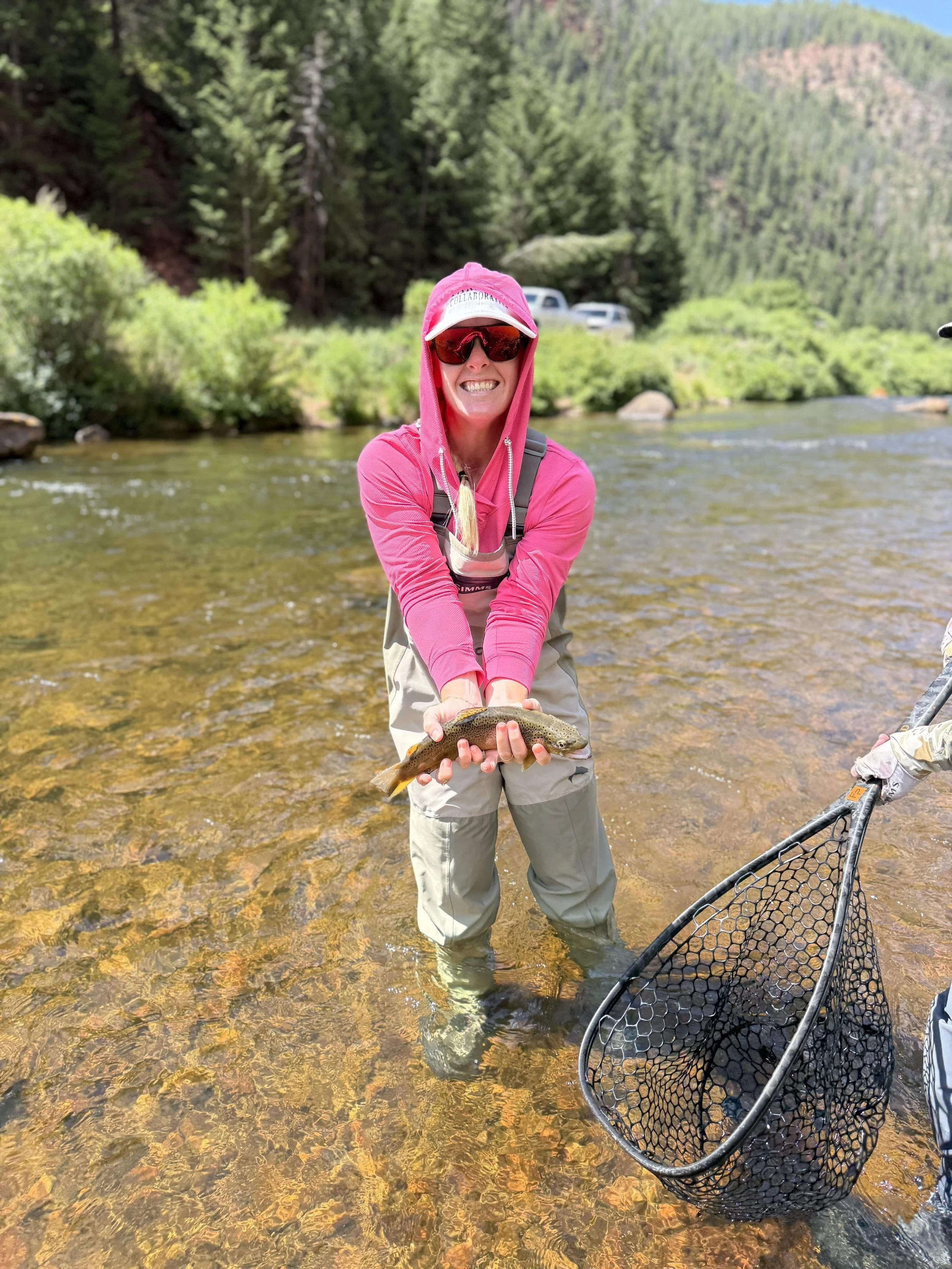 Kat Libby wellness coach holding a fish she has caught in a river