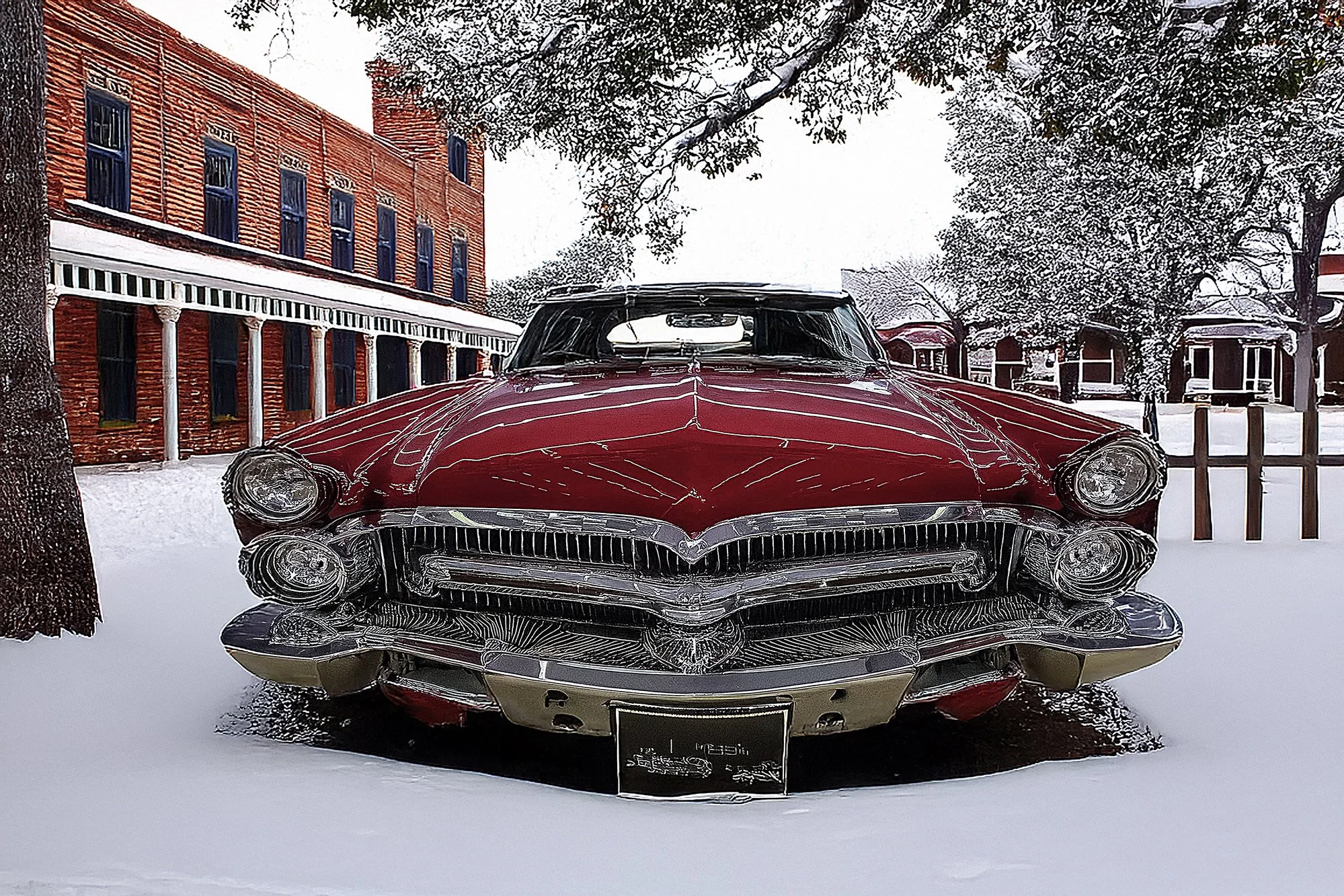 Front view of a vintage red car parked on snow with a red brick building and snowy trees in the background.