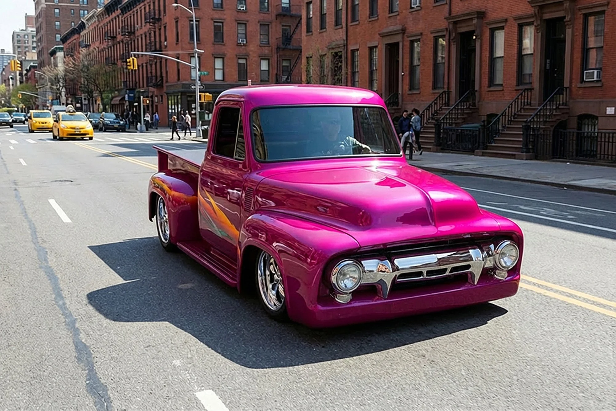 A pink vintage pickup truck driving on a city street with brick apartment buildings and pedestrians in the background.