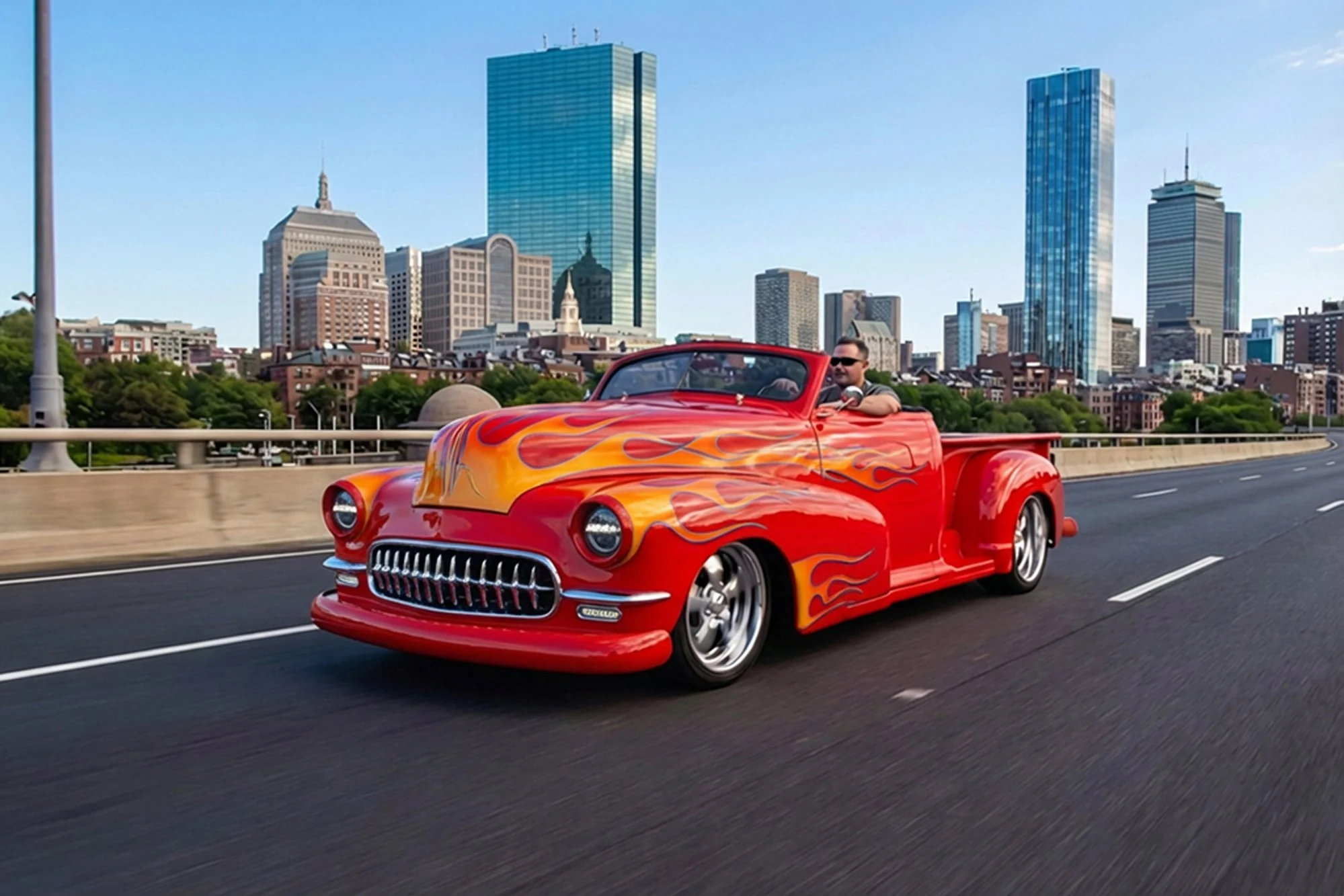 A man driving a red vintage convertible car with flame decals on the hood on a city highway, with skyscrapers in the background.