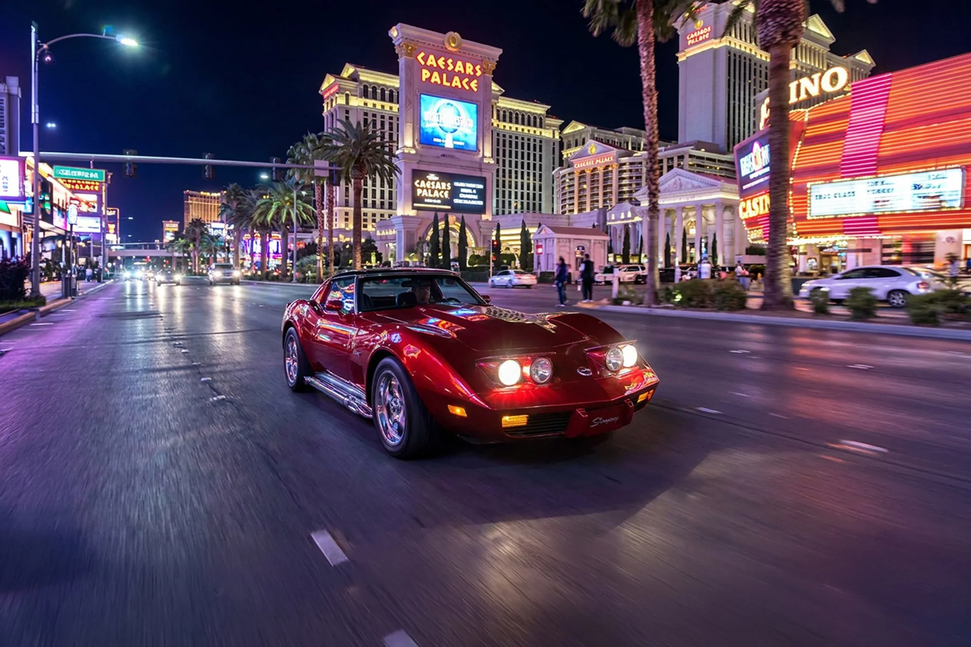 A red sports car driving down a busy city street at night, with bright neon signs and casinos in the background, including Caesars Palace.