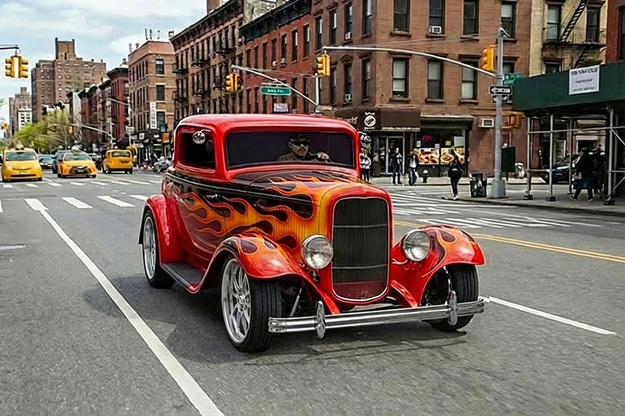 Red vintage hot rod car with flame decals on the hood driving down a city street, with pedestrians, yellow taxis, and brick buildings in the background.