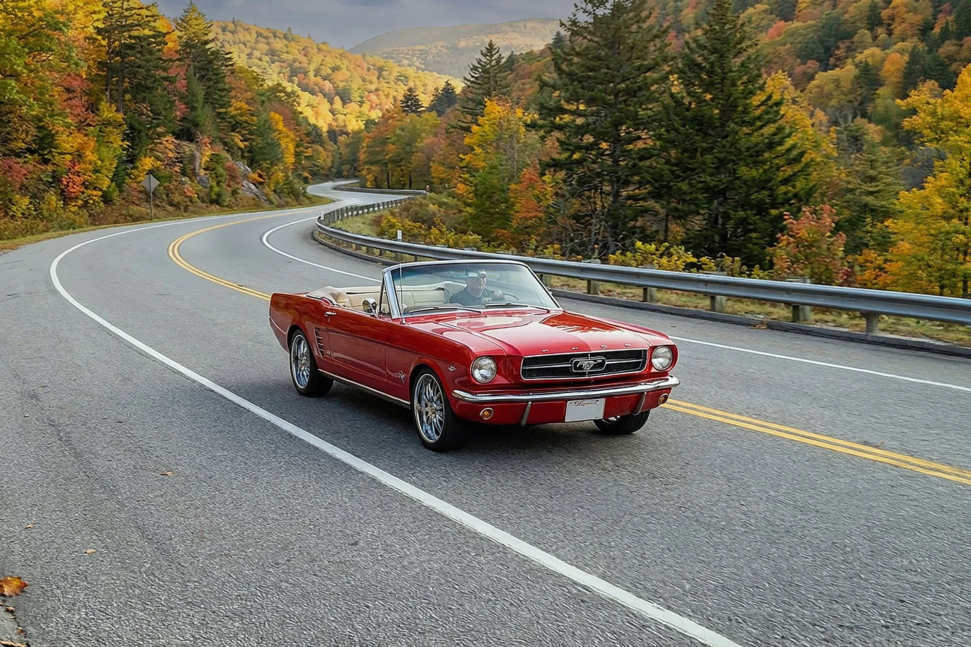 Red vintage convertible Ford Mustang driving on a winding mountain road surrounded by autumn trees.