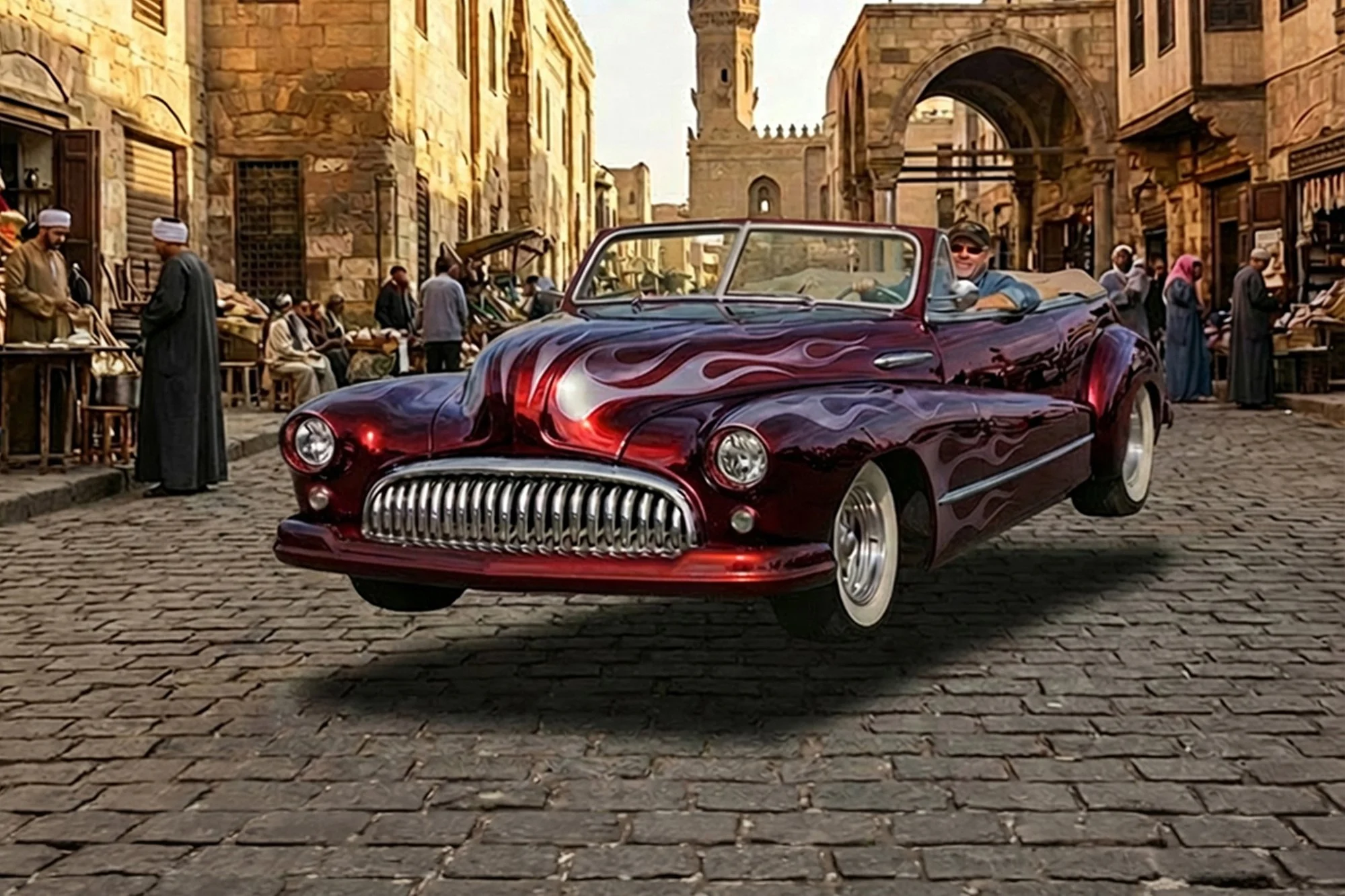 A vintage red and black car with flame decals on the hood driving on cobblestone street in an old city, with people in traditional dress and historic architecture in the background.