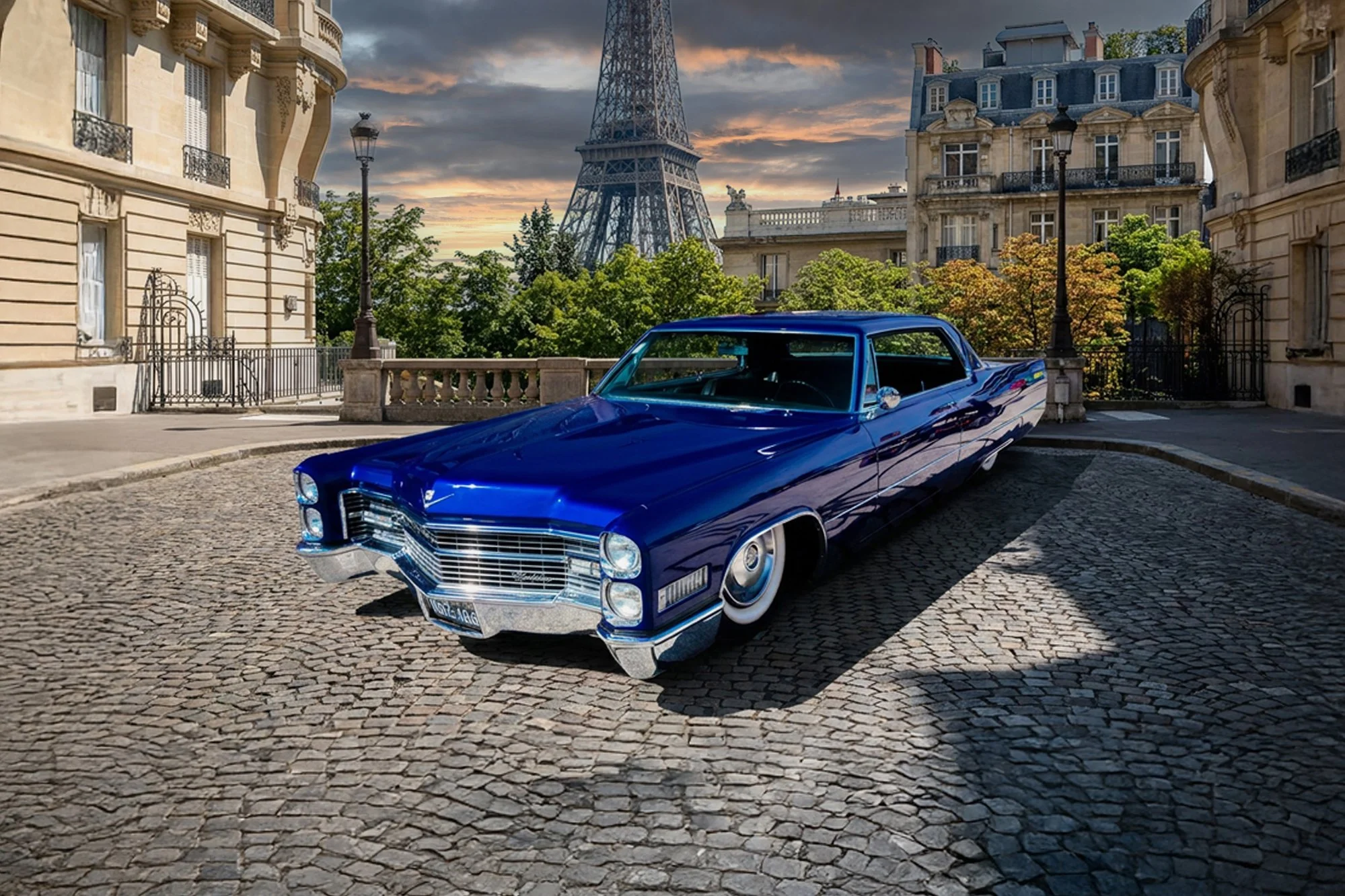 A shiny, vintage blue Cadillac parked on a brick-paved street in a Paris neighborhood with classic European architecture, lamp posts, trees, and the Eiffel Tower in the background during sunset.