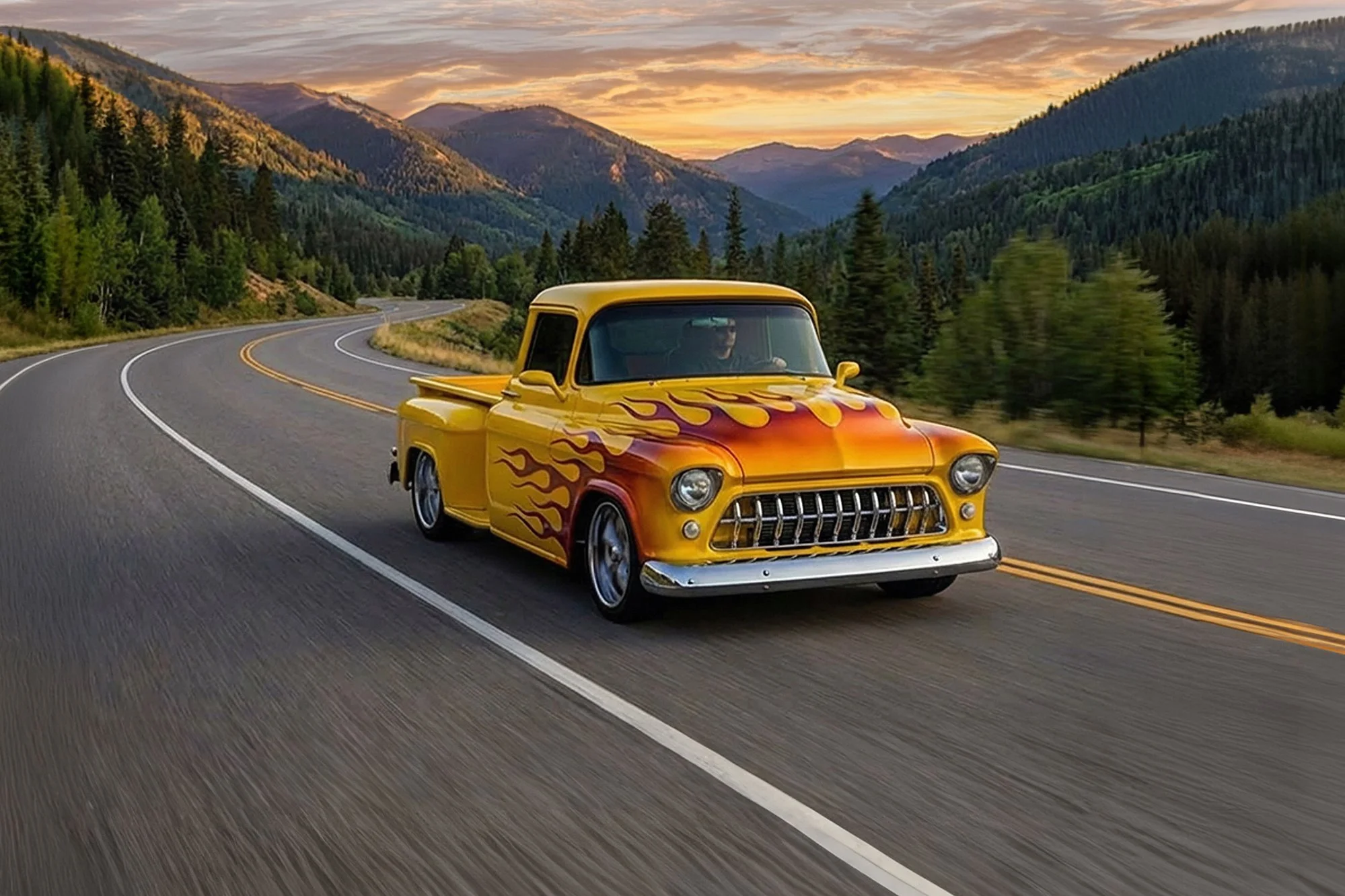 A bright yellow vintage pickup truck with flame decals on the hood driving on a winding mountain road at sunset, surrounded by green pine trees and mountain scenery.