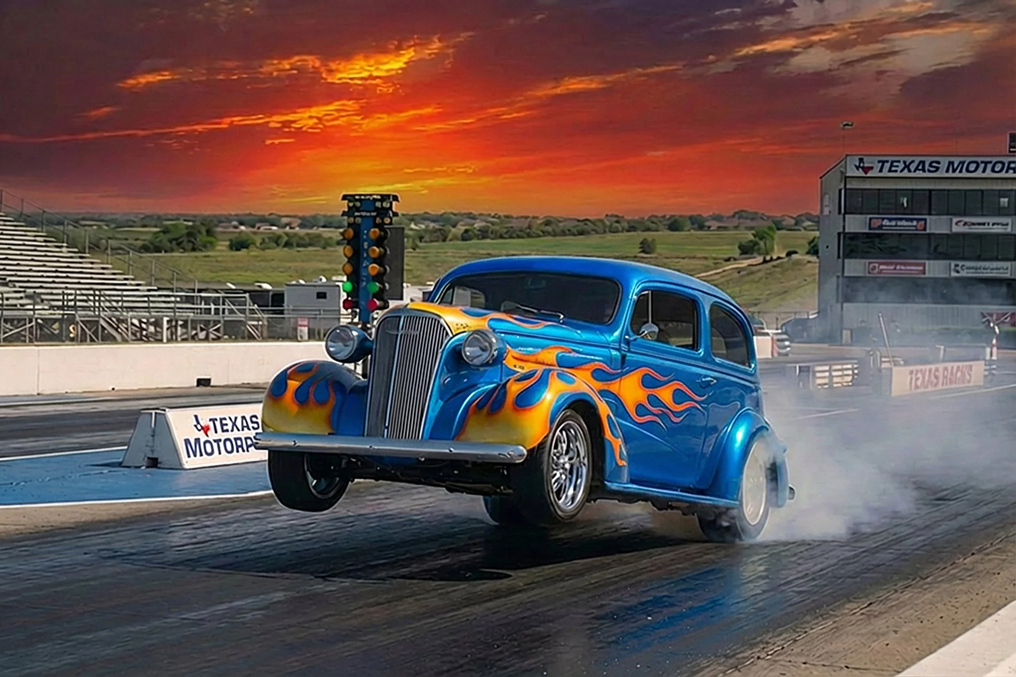 A vintage blue car with orange flame decals on the hood and sides is racing on a drag strip, kicking up smoke. The background features a sunset sky with orange and purple hues, a racing track setup with a starting tree, and a sign for Texas Motorplex