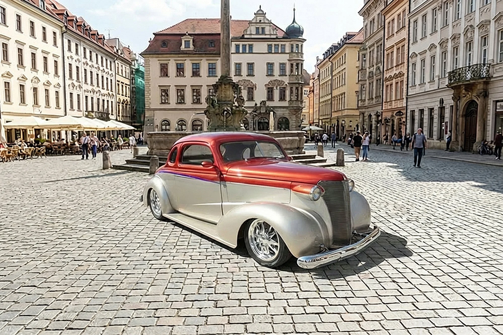 A vintage silver and red car parked on cobblestone pavement in a European square with historic buildings and people walking in the background.