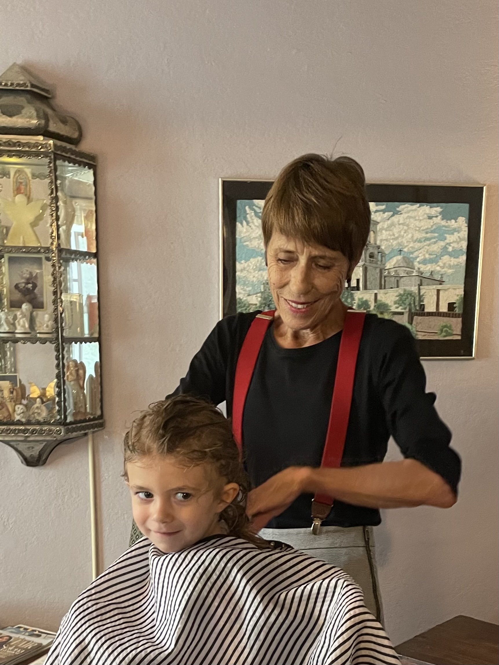 A woman giving a haircut to a young girl sitting in a salon chair.