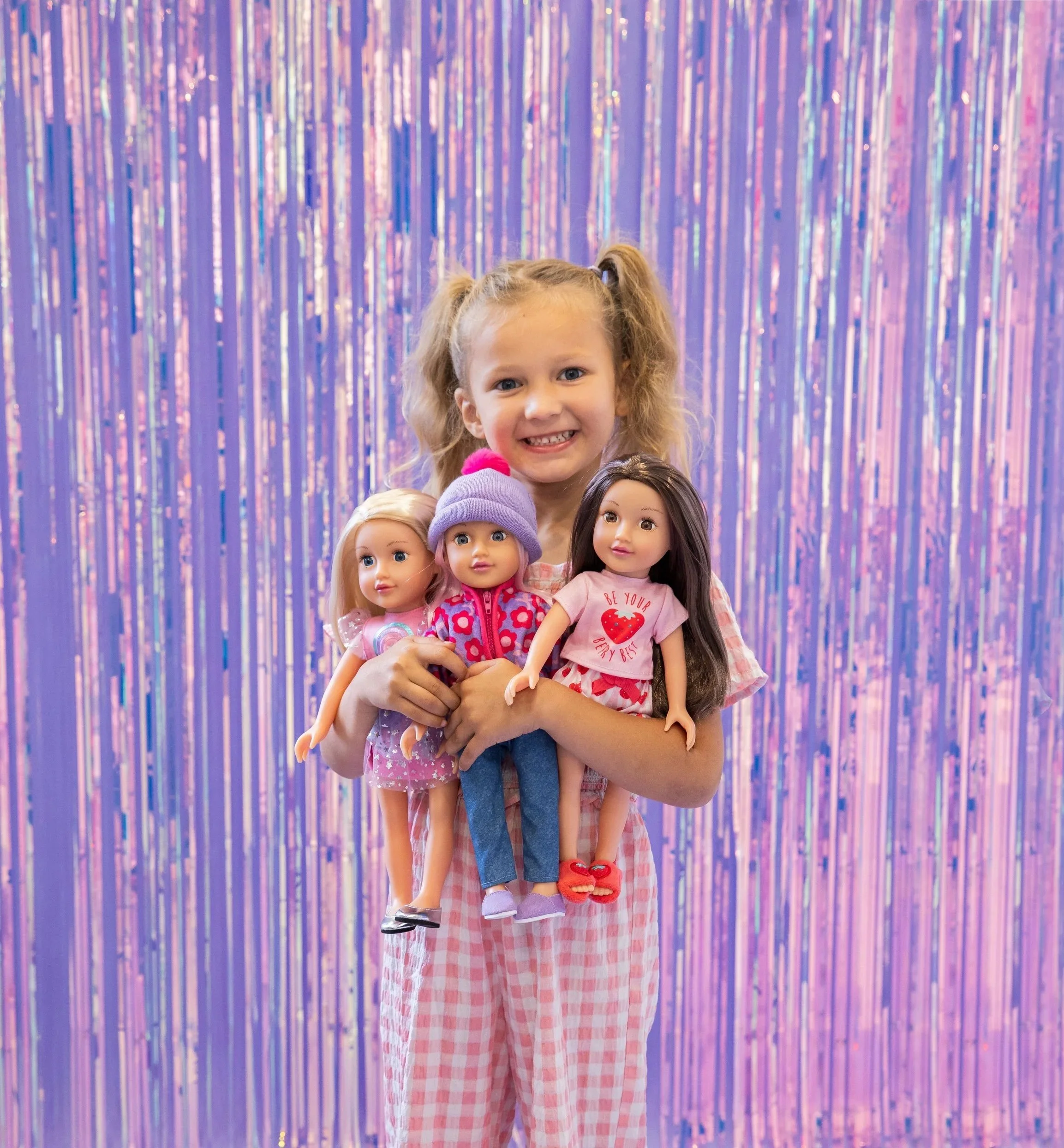 A young girl smiling while holding her three favourite 14 inch Little Sister designAfriend dolls.