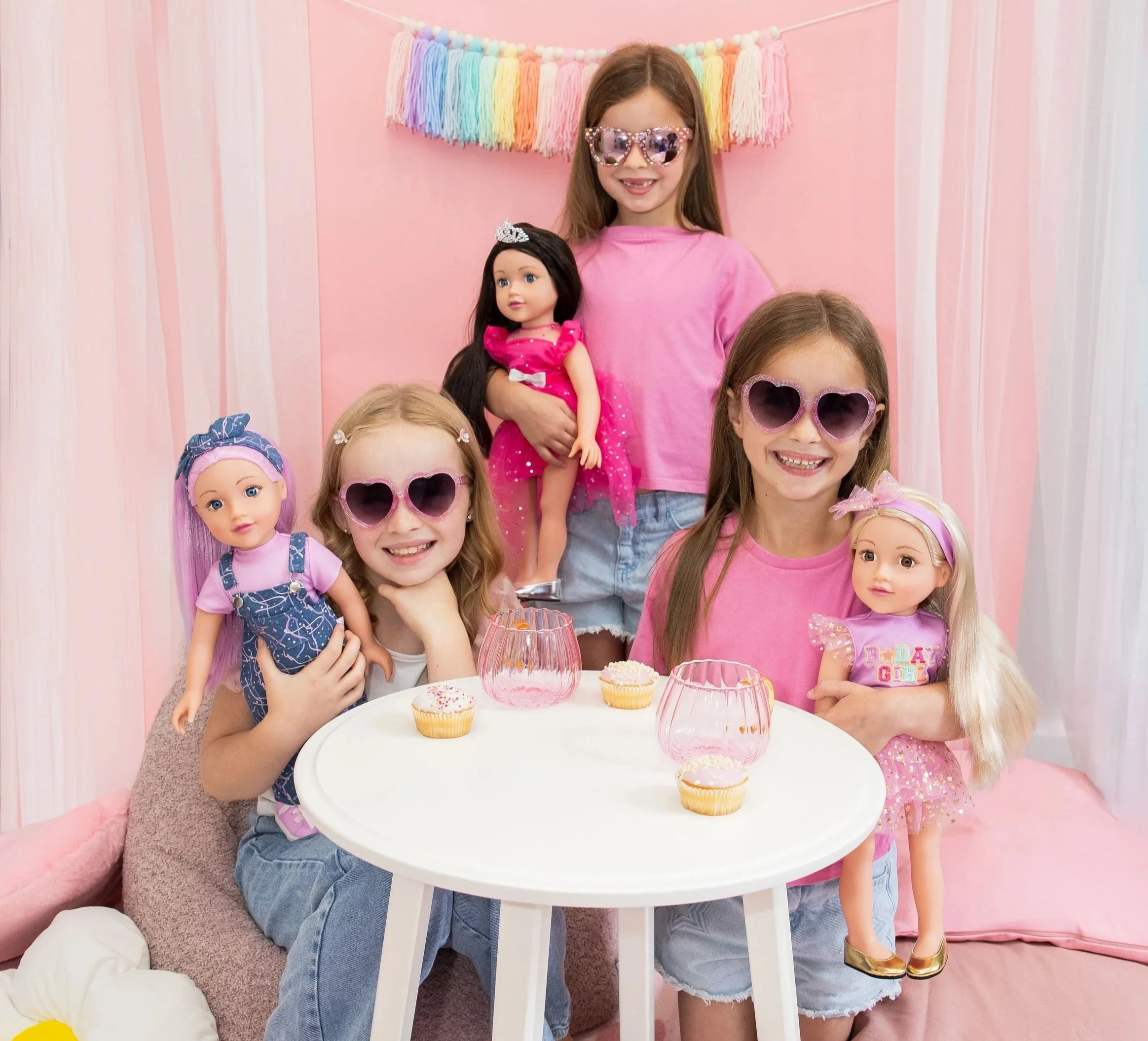 Three girls wearing playful heart sunglasses, posing for the camera, holding their favourite 18 inch DesignAfriend doll.