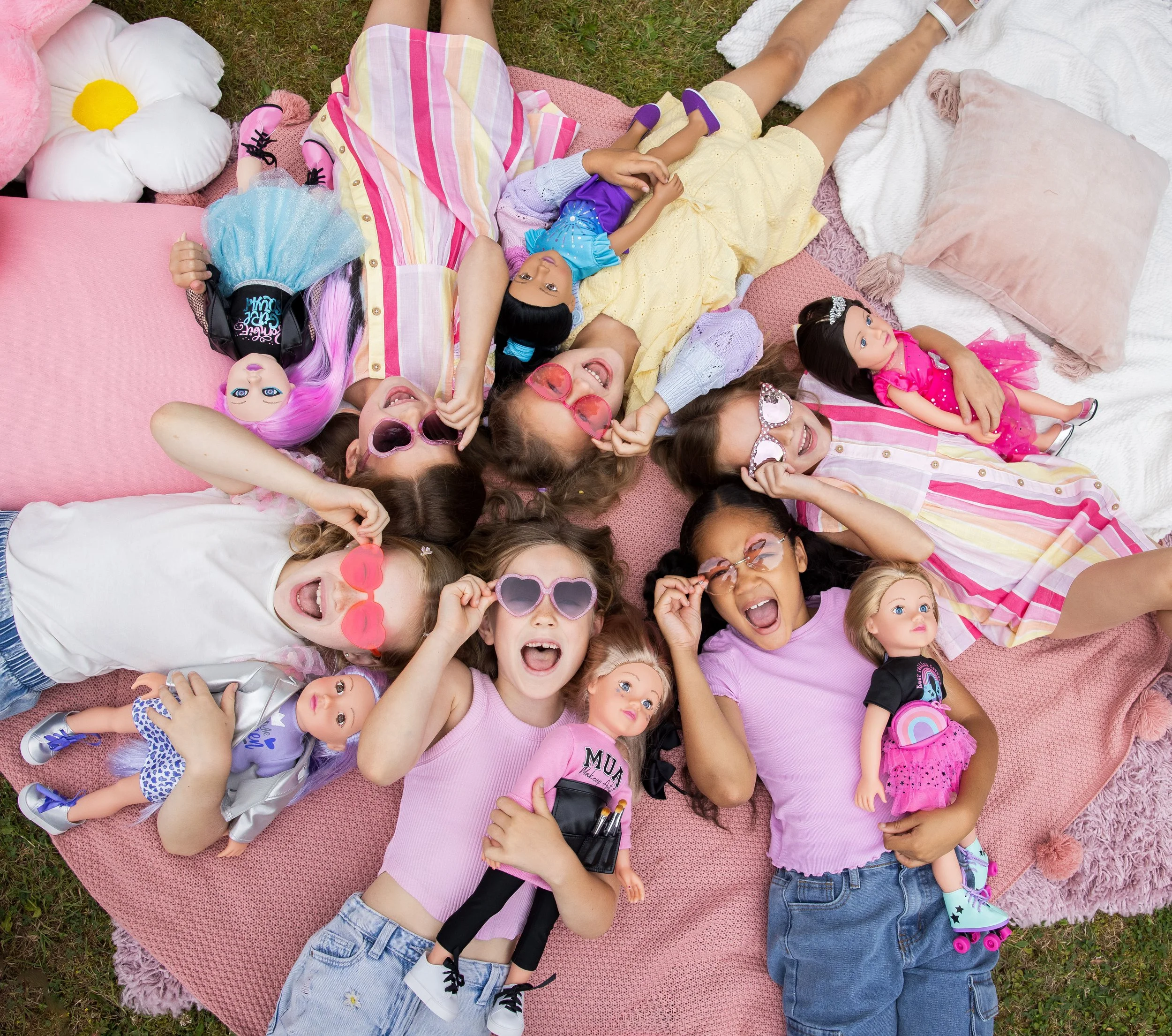 Group of girls lying on the floor, looking up at the camera smiling and laughing, each holding their favourite DesignAfriend doll.