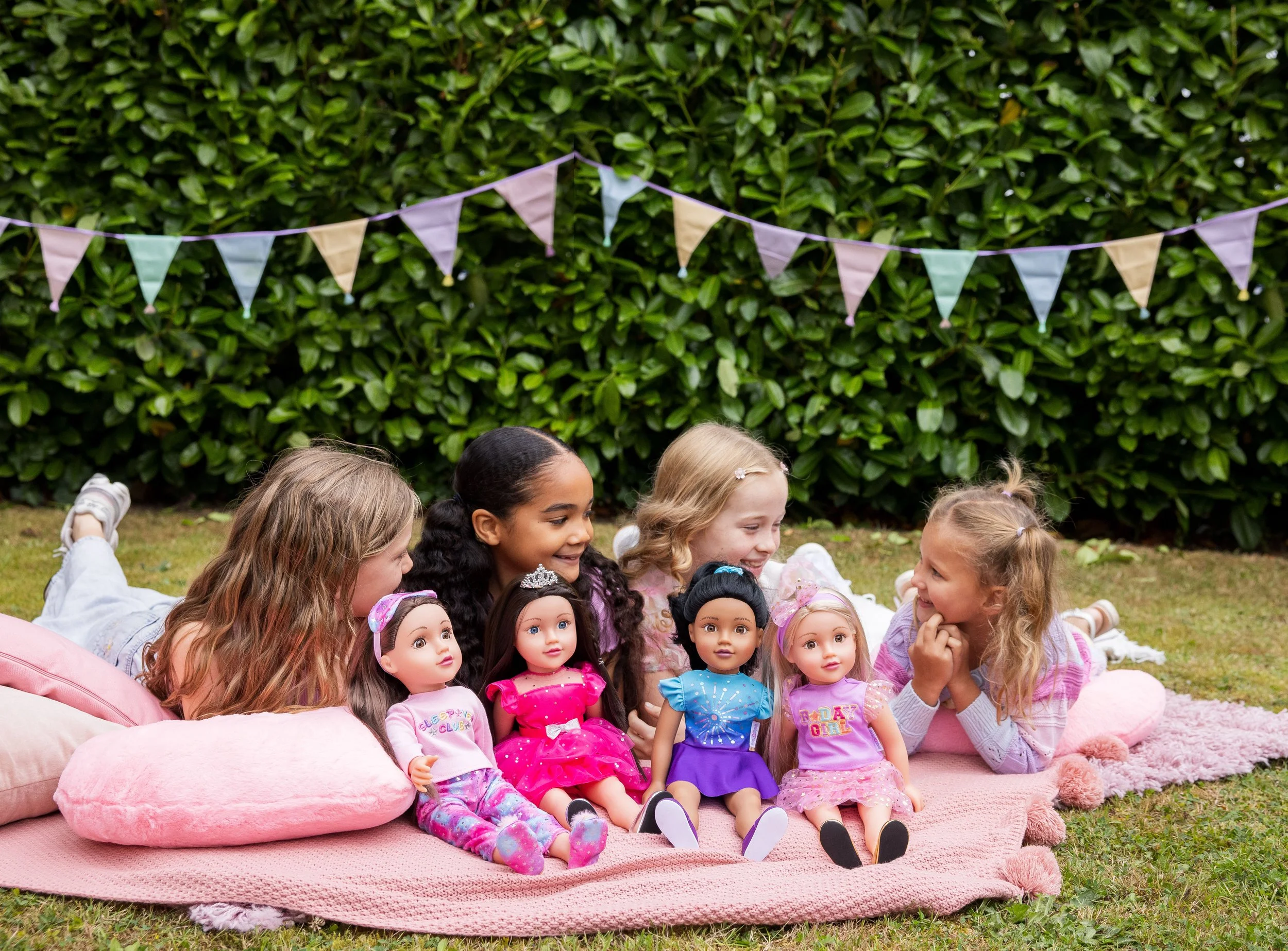 Four girls sat outside chatting and smiling whilst holding their favourite 18 inch DesignAfriend doll.