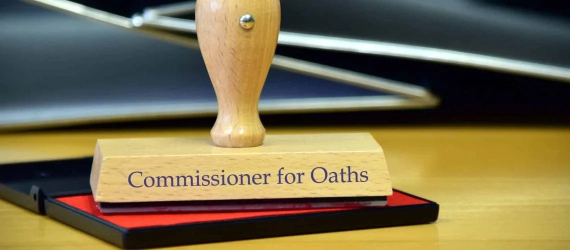 A wooden stamp with the text "Commissioner for Oaths" on it, resting on a red and black tray.