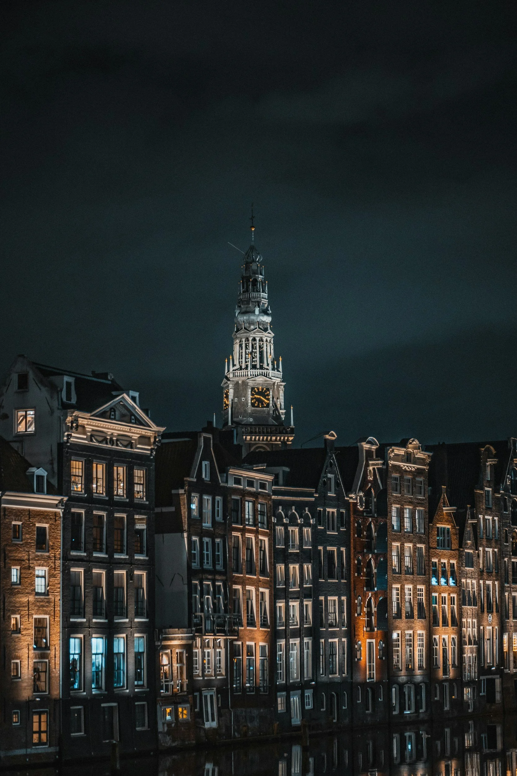 Aufnahme einer Stadt bei Nacht, showing alte Gebäude mit beleuchteten Fenstern und einen hohen Kirchturm im Hintergrund.