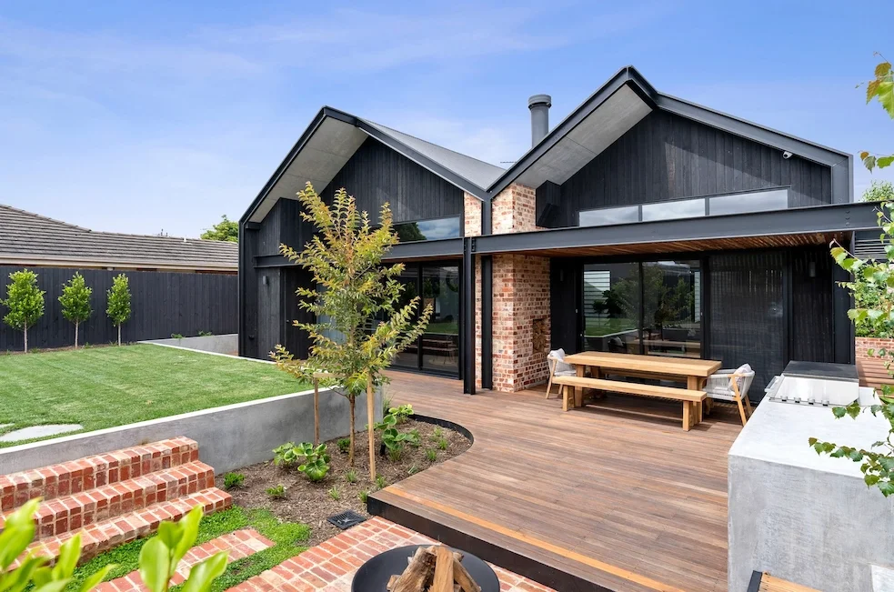 Contemporary custom home in Geelong designed by Homes By NH with black exterior cladding, timber deck, landscaped yard, and large glass windows.