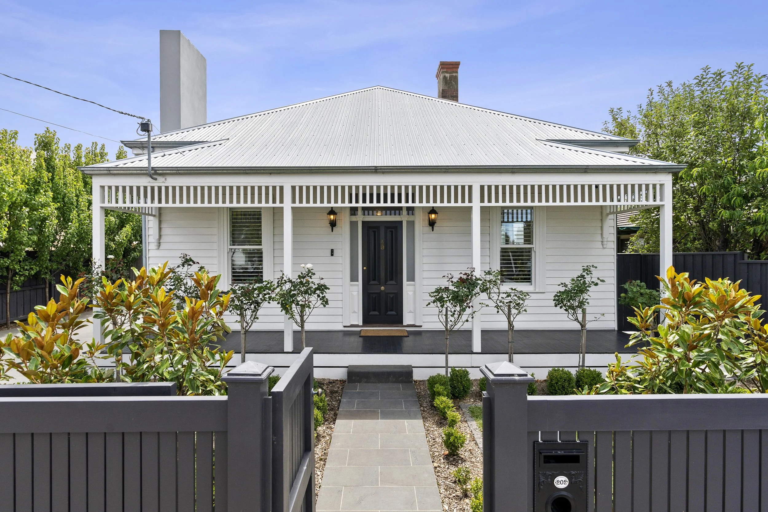 Renovated white weatherboard home in Geelong West with black front door, front porch lighting, and landscaped walkway built by Homes By NH