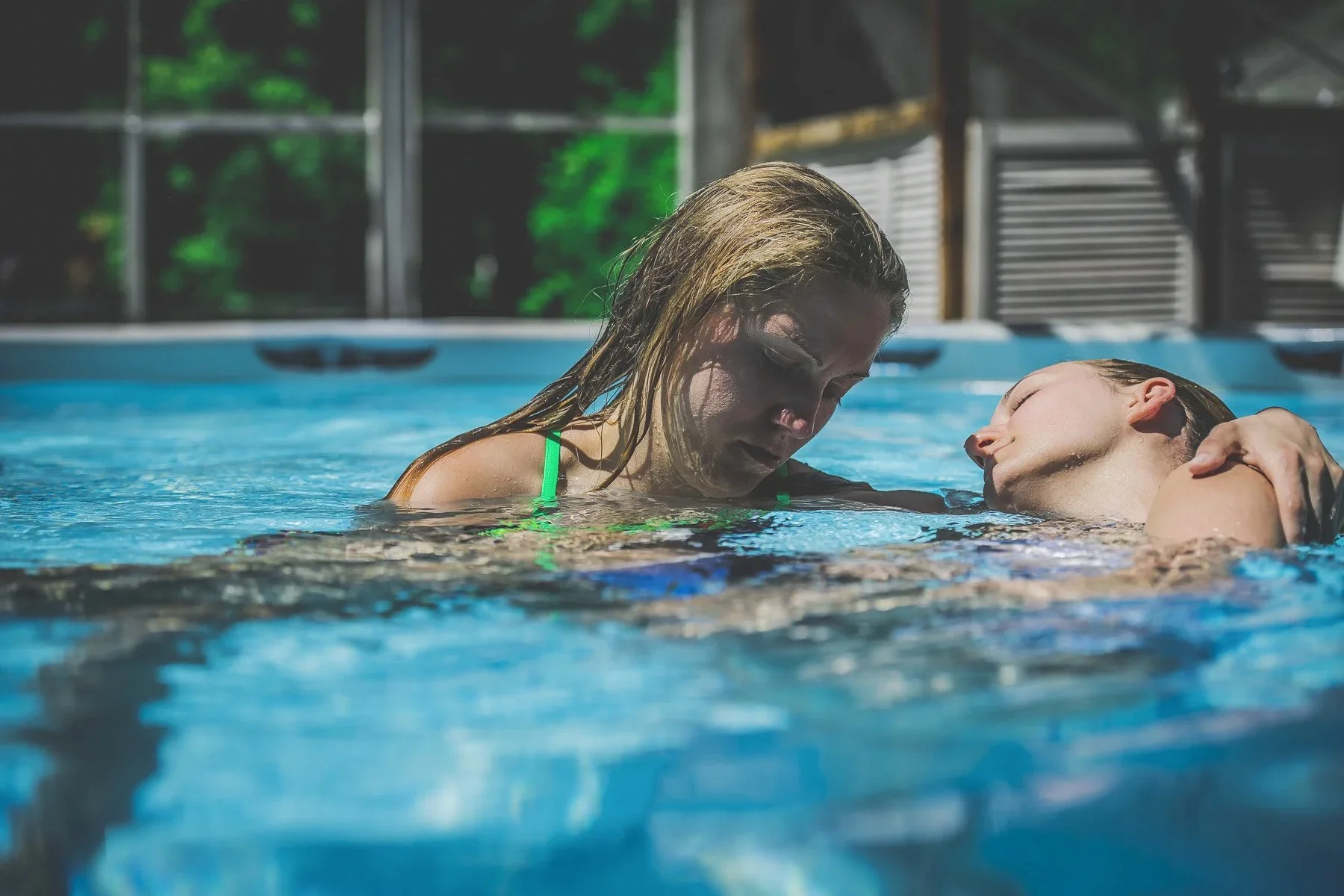 A woman with long wet hair holding a young person in a swimming pool, with trees visible outside the window in the background.
WATSU aquatic bodywork and therapy , hydrotherapy , deep relaxation , nervous system regulation