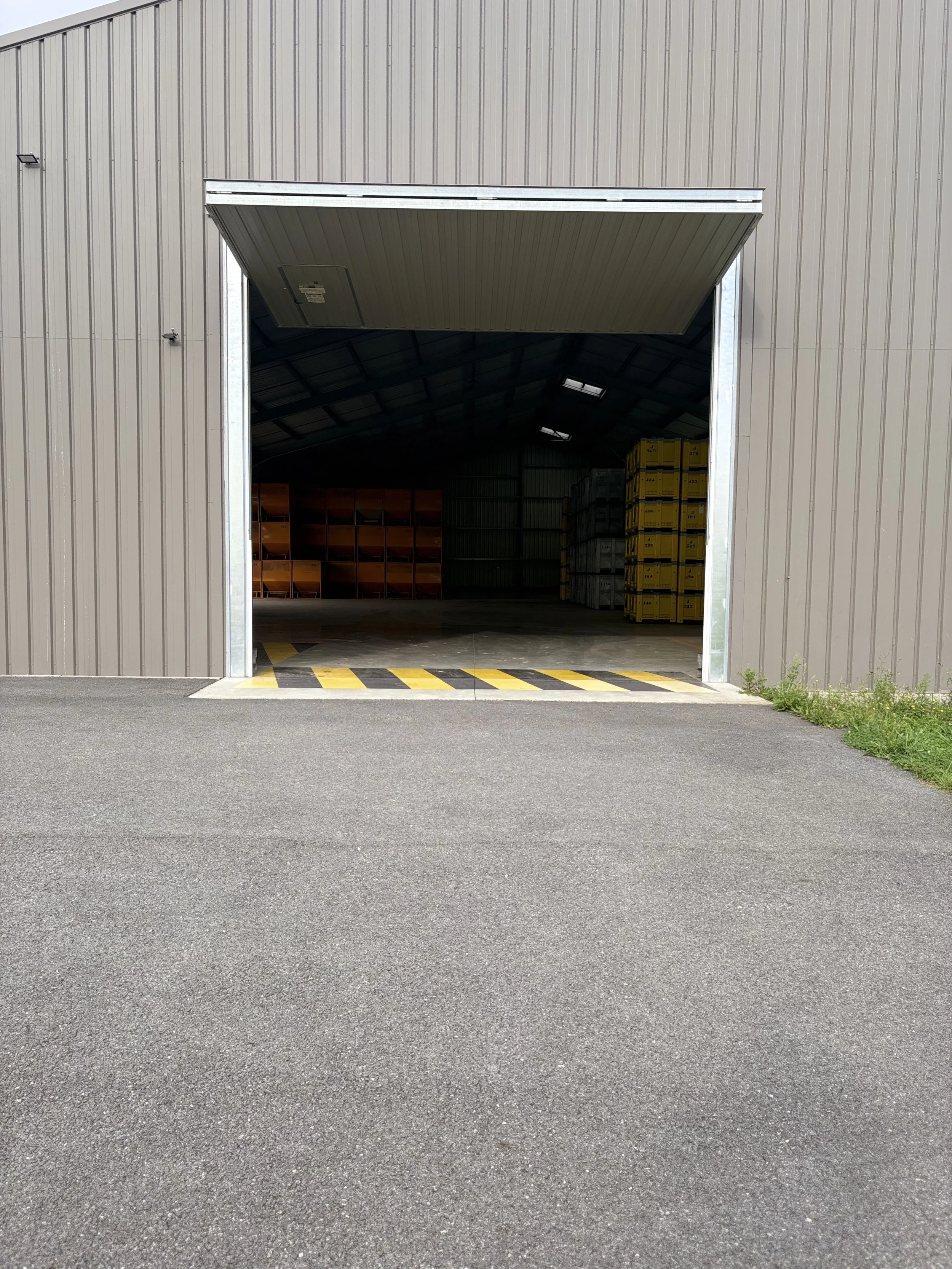 Open warehouse door with stacked storage containers inside, yellow and orange crates, and a gray metal roof.