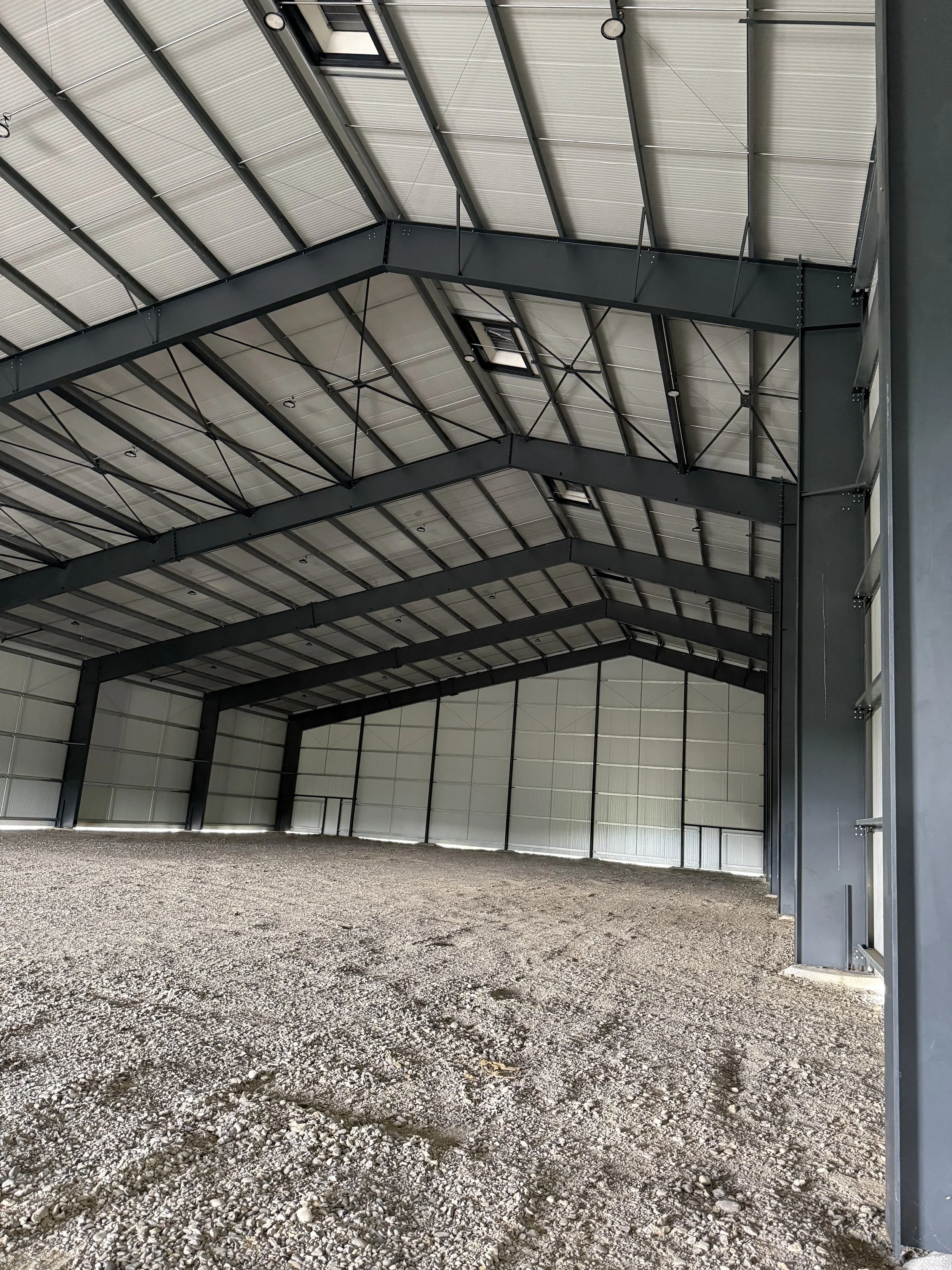 Inside a large, empty metal warehouse with a gravel floor and high ceiling.