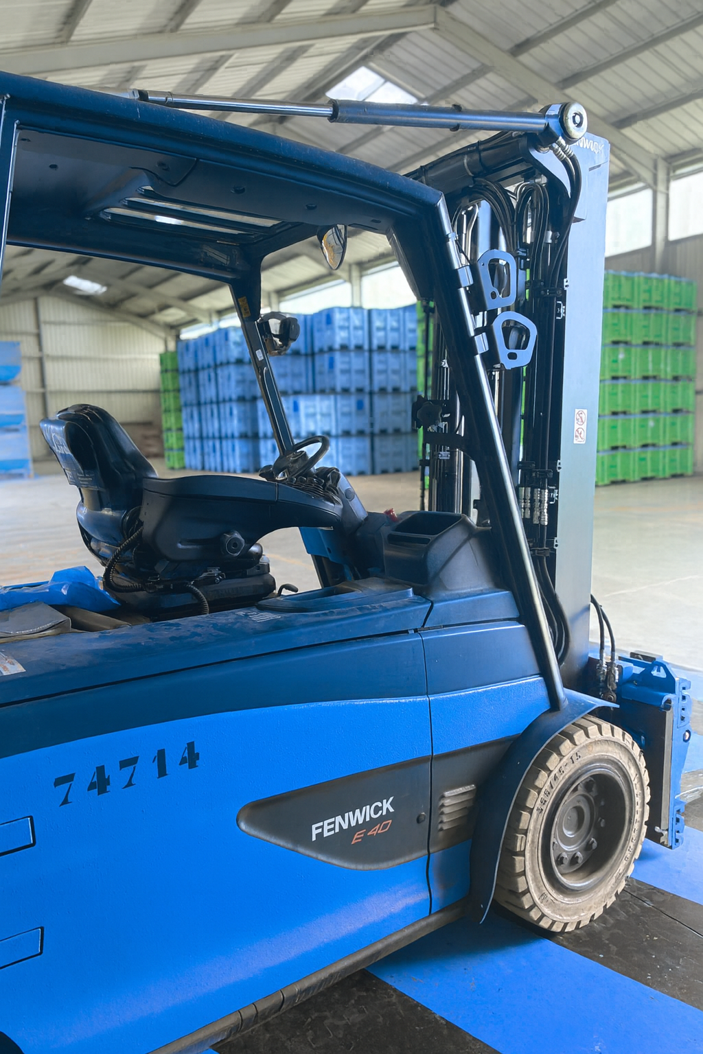 Blue Fenwick E40 forklift inside a warehouse with stacks of blue and green plastic crates in the background.