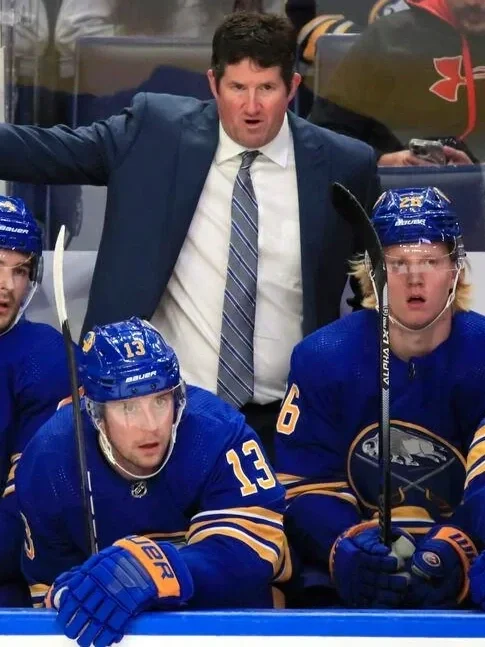 Marty Wilford Ice hockey coach in a suit giving instructions to players on the bench during a game.