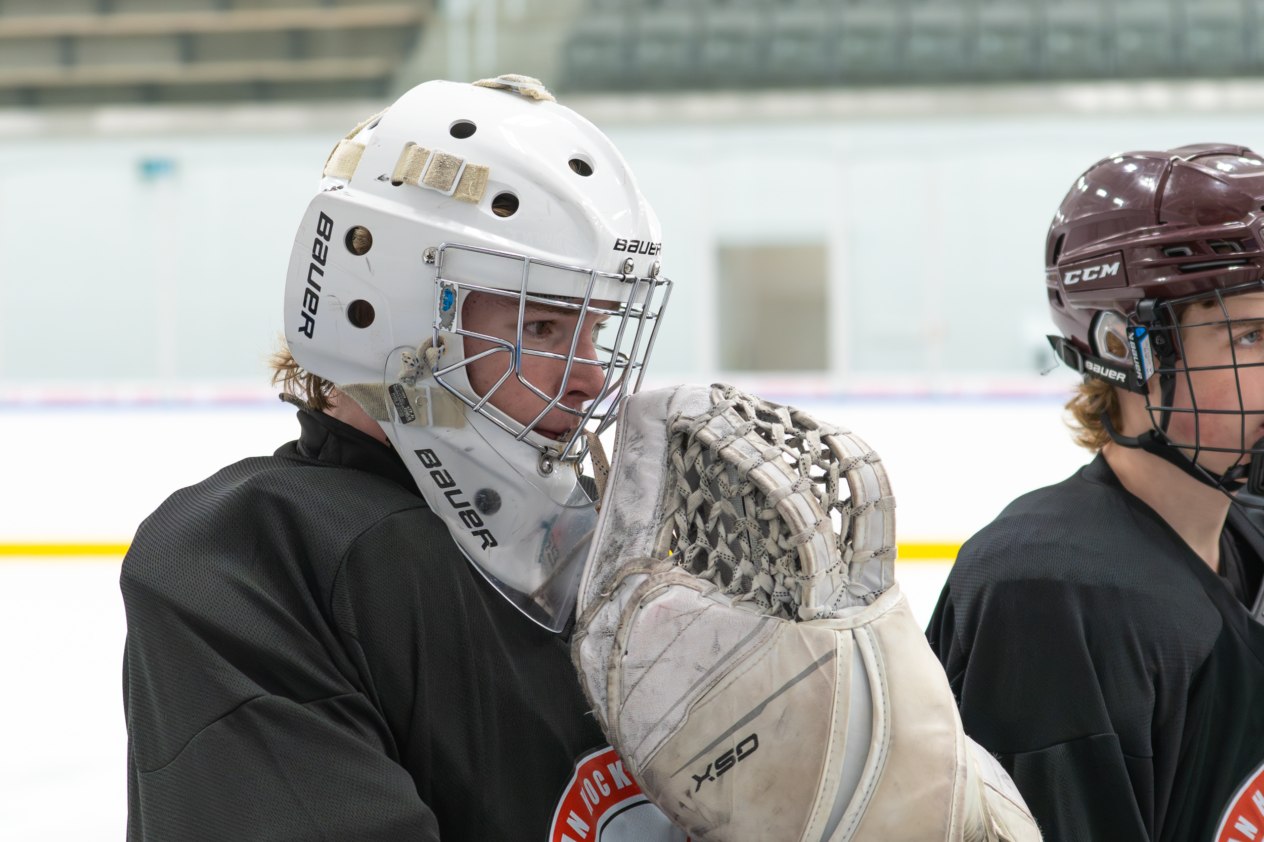 Hockey players wearing helmets and jerseys on the ice rink, one player adjusting their glove.