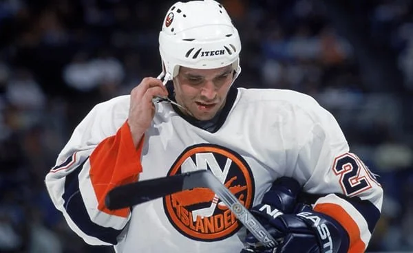 Ice hockey player in white and orange jersey with number 22, wearing a helmet, looking down, holding a hockey stick, on ice rink.